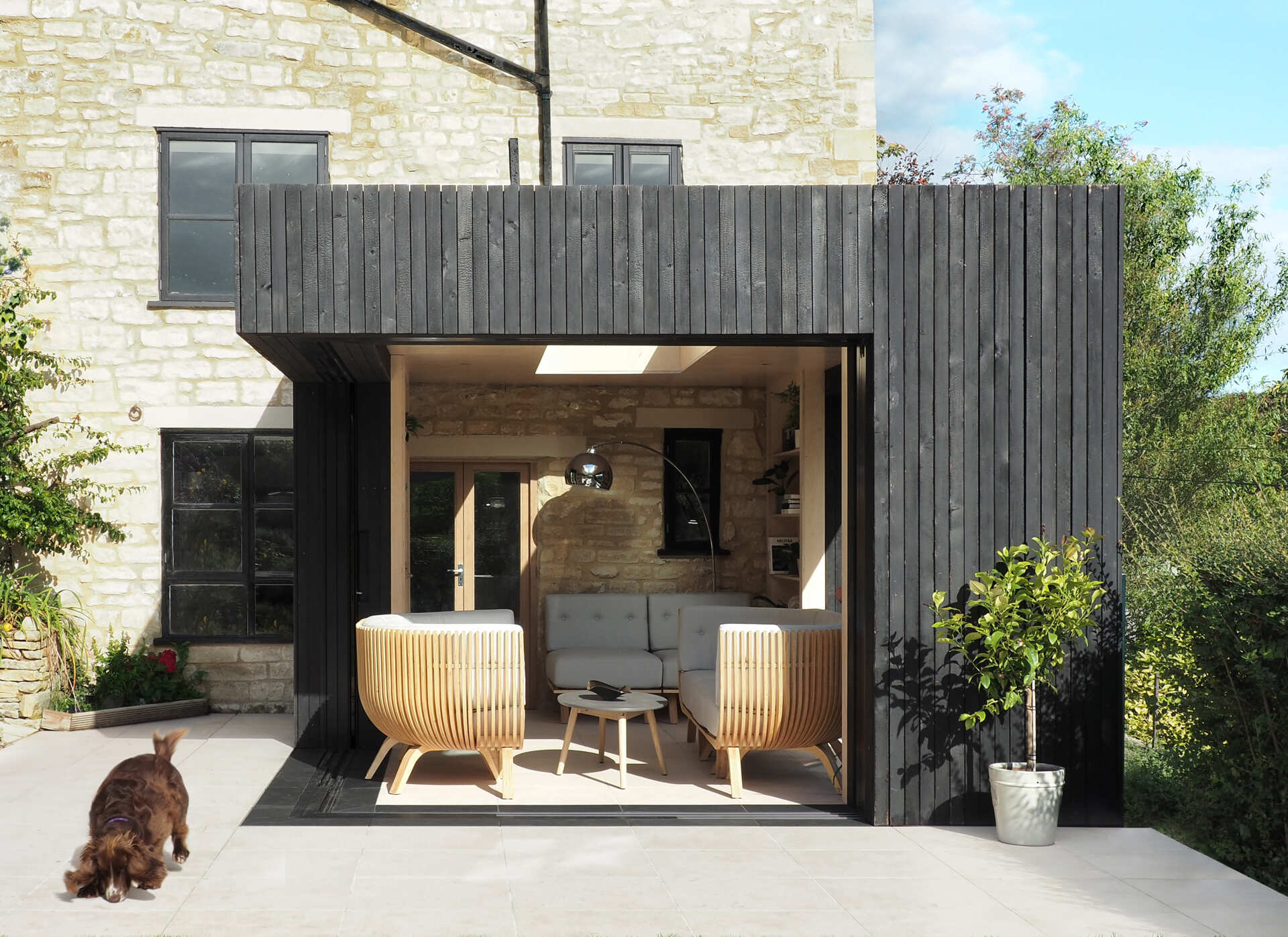A historic Cotswold cottage meets modern design with charred timber, black frames, and disappearing glass walls that open straight onto the garden.