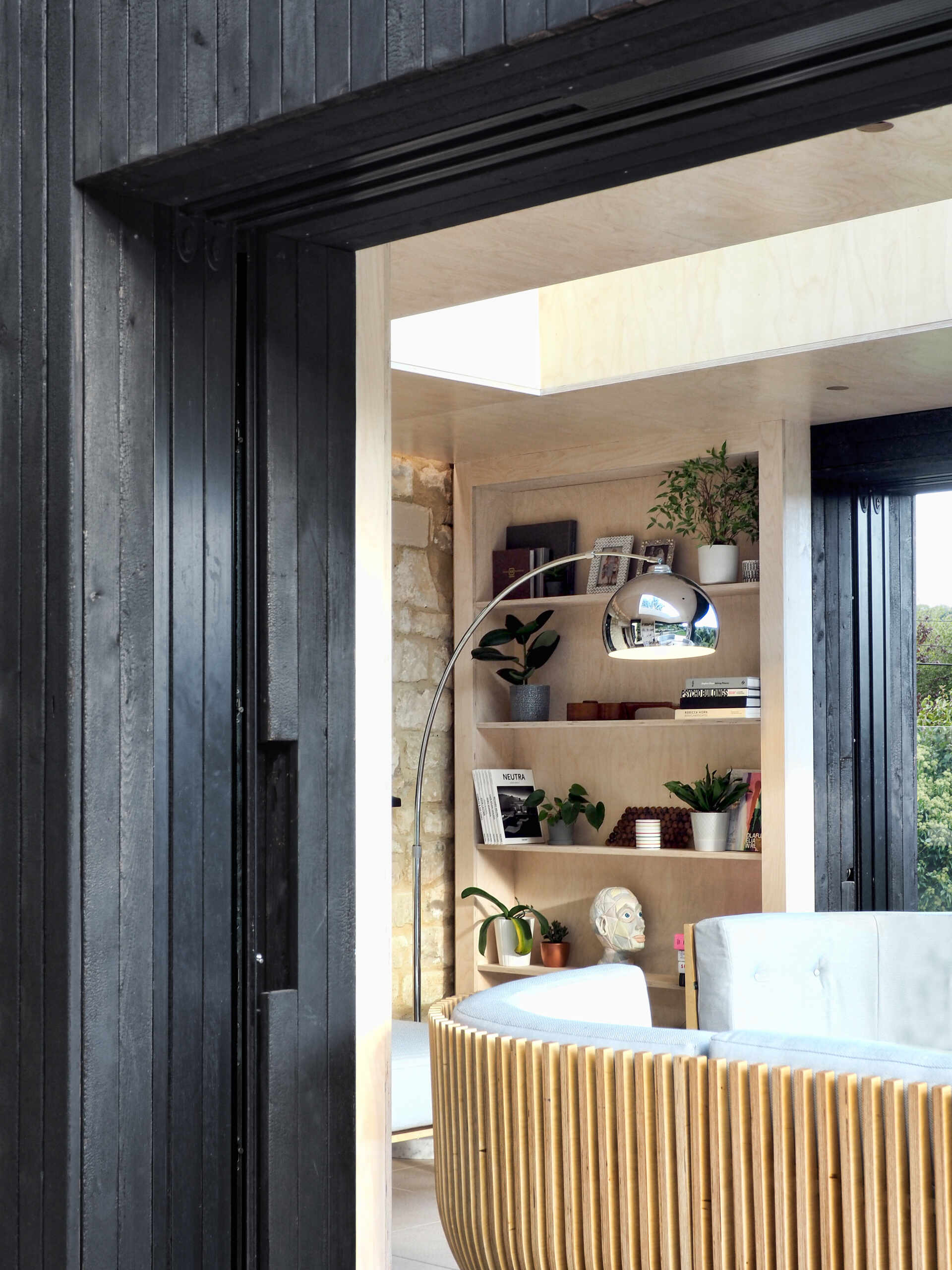 Una cabaña histórica de Cotswold combina un diseño moderno con vigas carbonizadas, marcos negros y paredes de vidrio que desaparecen y se abren directamente al jardín.