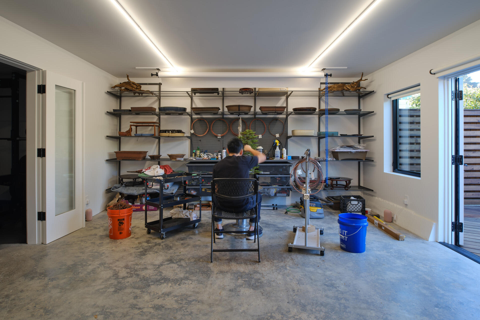 The renovation introduces a dedicated workshop environment with wide French doors opening from street to garden. Large carts can move bonsai trees directly from truck to backyard with ease, while still accommodating a single car garage.