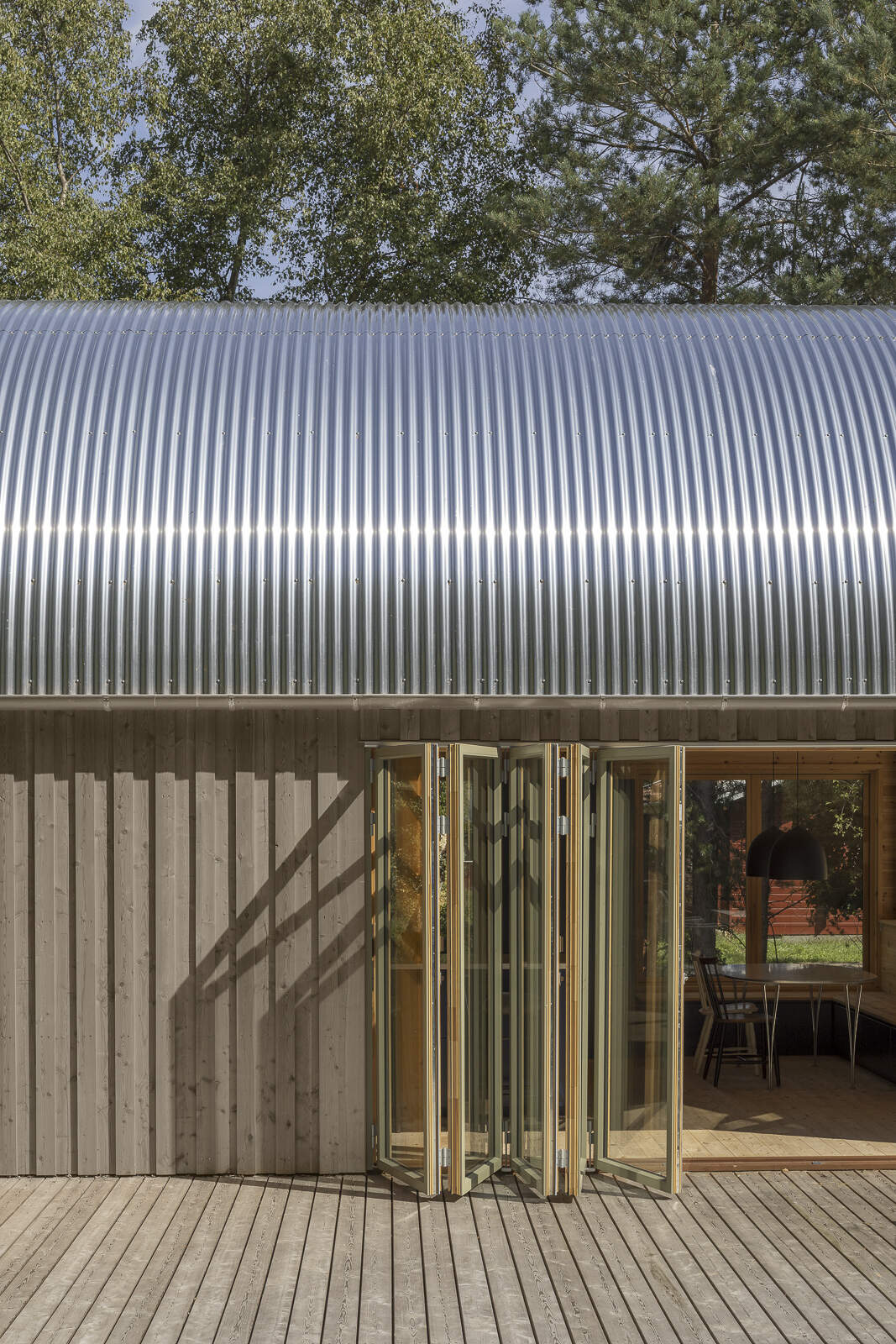 A tube-shaped Danish summer home set in the forest just 200 metres from the sea, featuring a curved corrugated steel roof and a bold minimalist form.