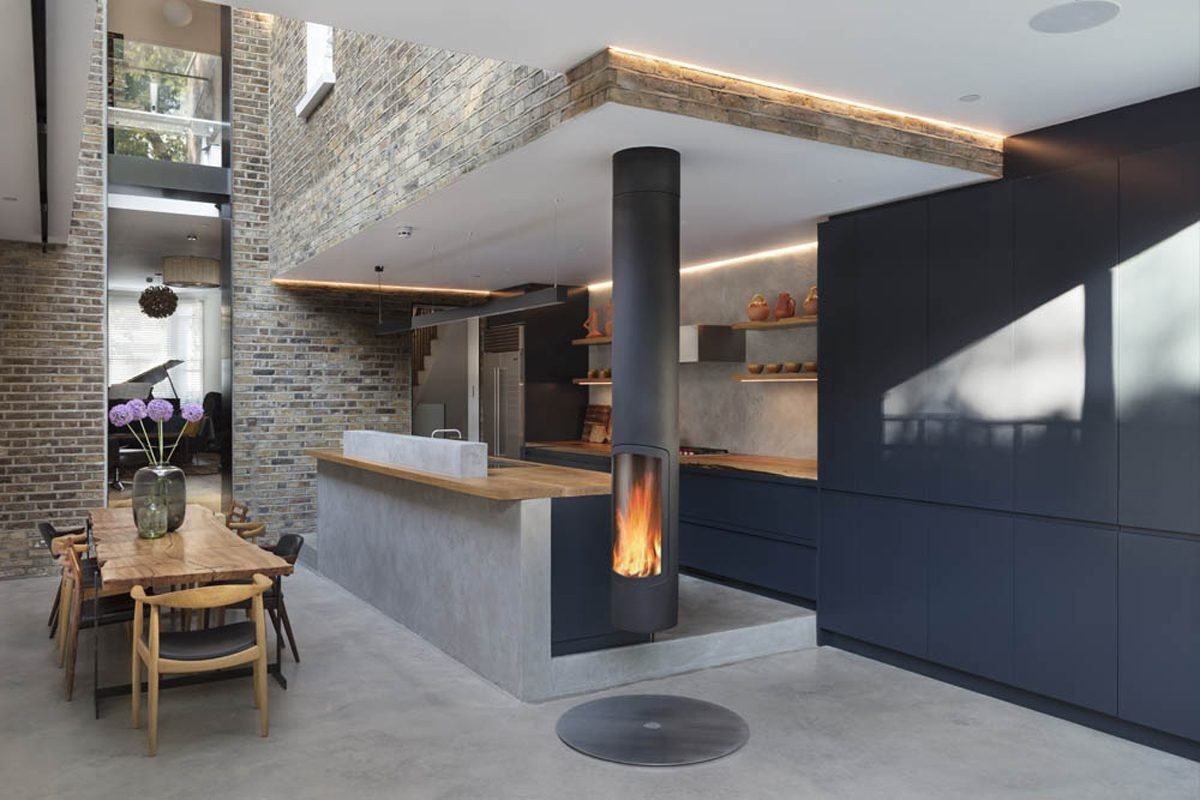A modern kitchen with dark cabinets, concrete floors and oak countertops sits at the heart of this open plan glass extension designed for entertaining.