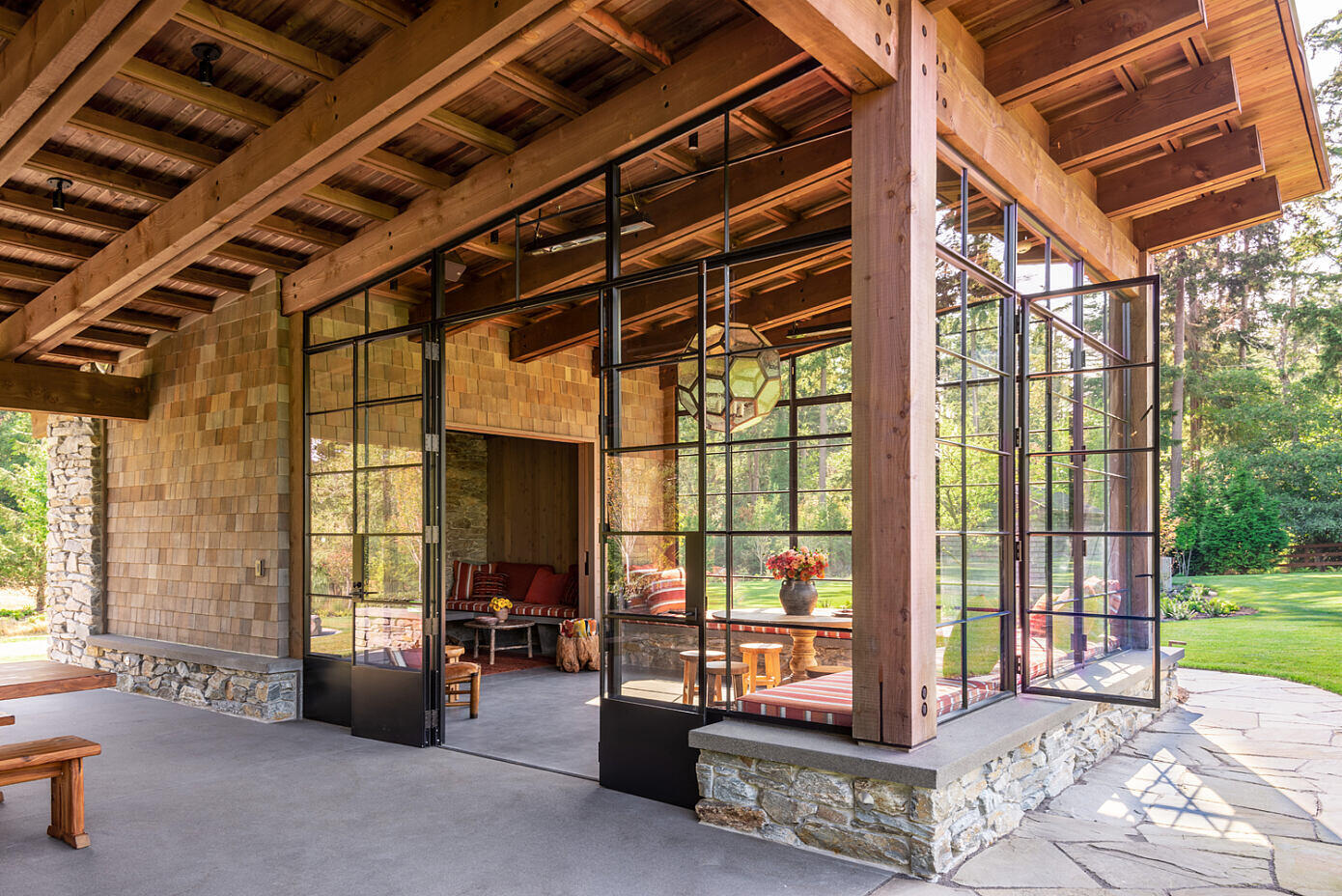 A light filled sunroom with wrap around seating flows into a cozy inglenook fireplace, creating intimate gathering spaces within the larger pavilion.