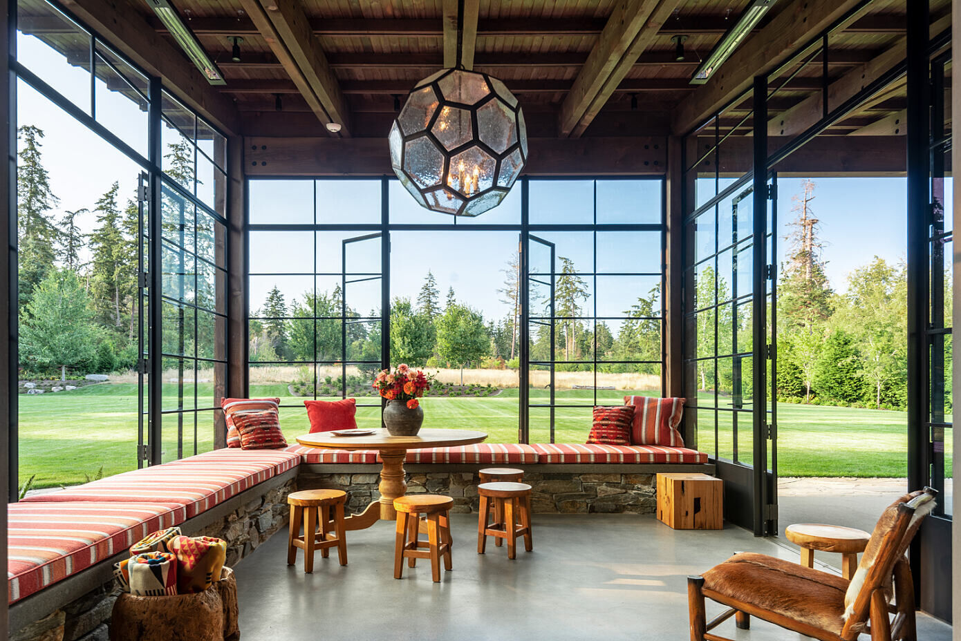 A light filled sunroom with wrap around seating flows into a cozy inglenook fireplace, creating intimate gathering spaces within the larger pavilion.