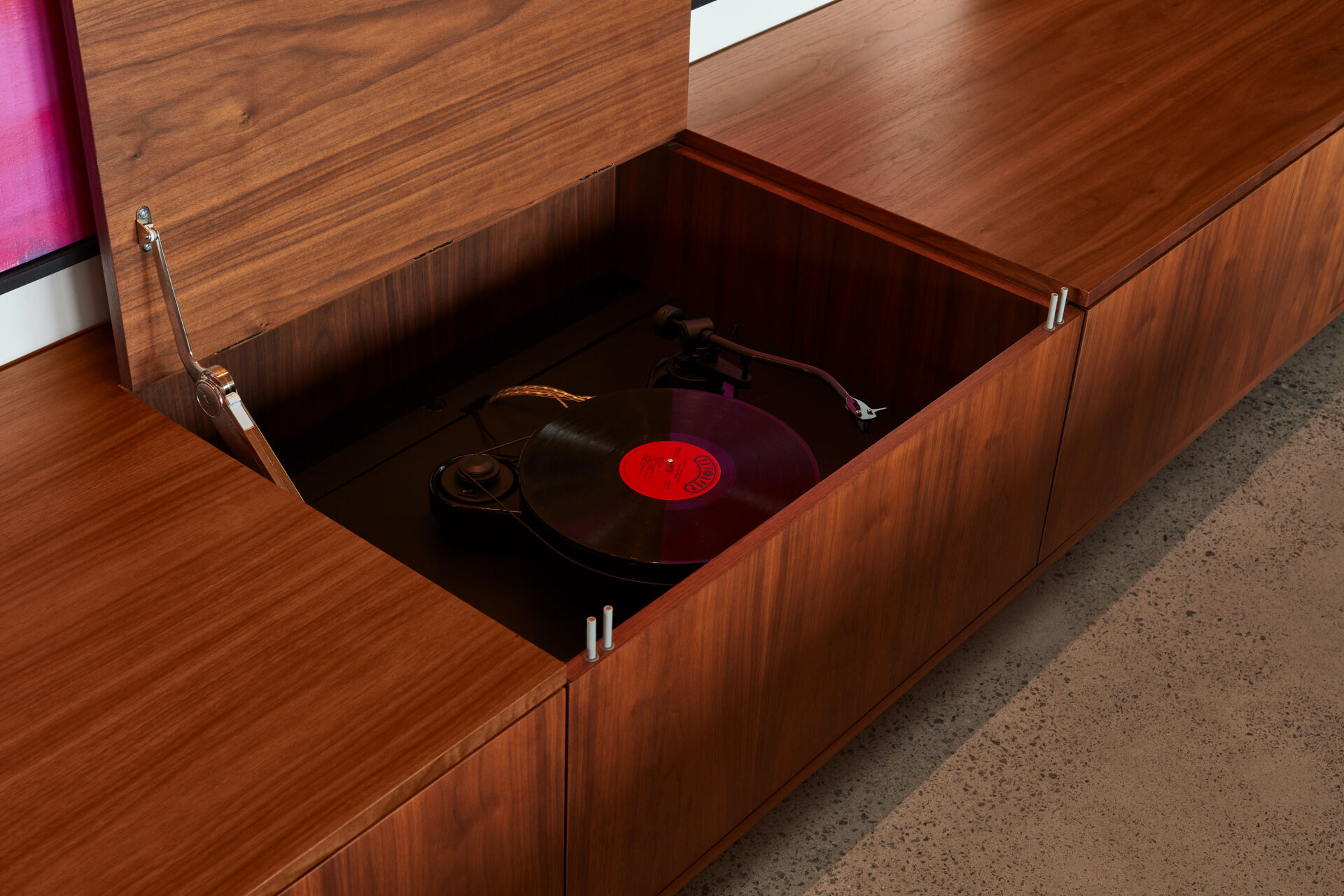 Las habitaciones se abren al paisaje y a los campos, favoreciendo el fácil movimiento entre el interior y el exterior. Un mueble bajo con un tocadiscos incorporado se alinea en la pared, añadiendo un toque personal a la sala de estar de planta abierta.