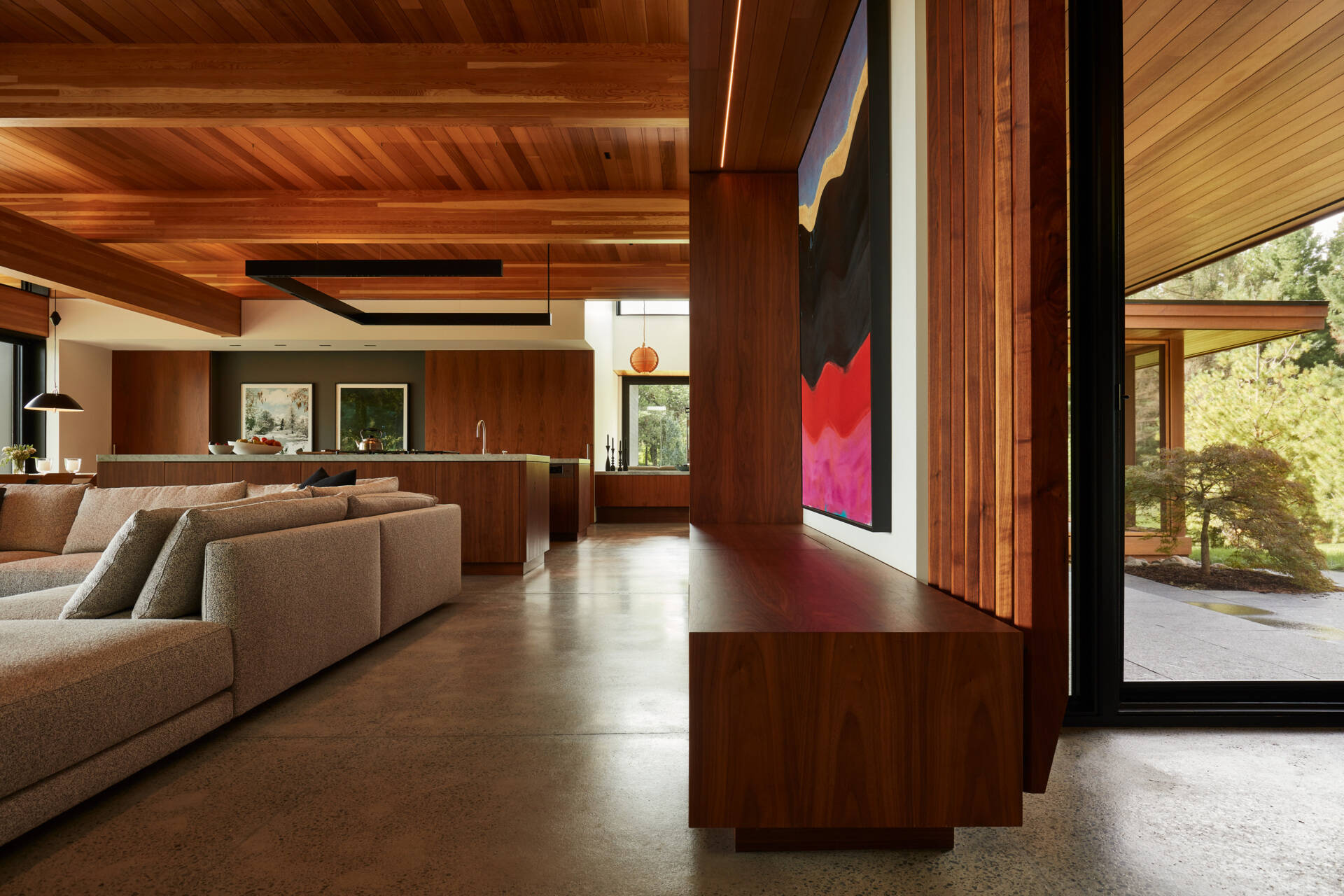 Las habitaciones se abren al paisaje y al campo, favoreciendo el fácil movimiento entre el interior y el exterior. Un mueble bajo con un tocadiscos incorporado se alinea en la pared, añadiendo un toque personal a la sala de estar de planta abierta.