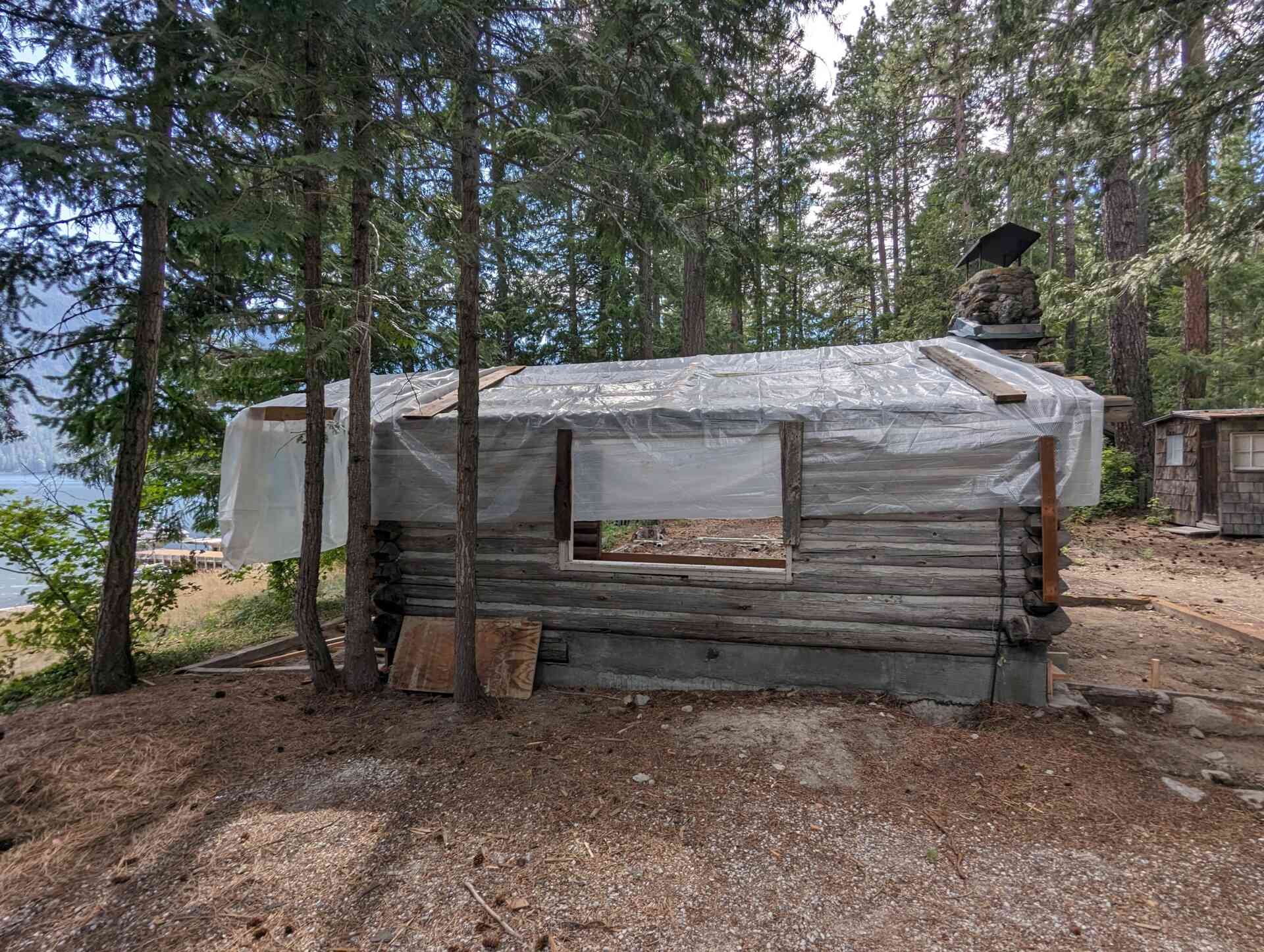 The original one-room log cabin from 1915 remains intact, revealing hand-hewn logs and a stone chimney beneath later additions. 