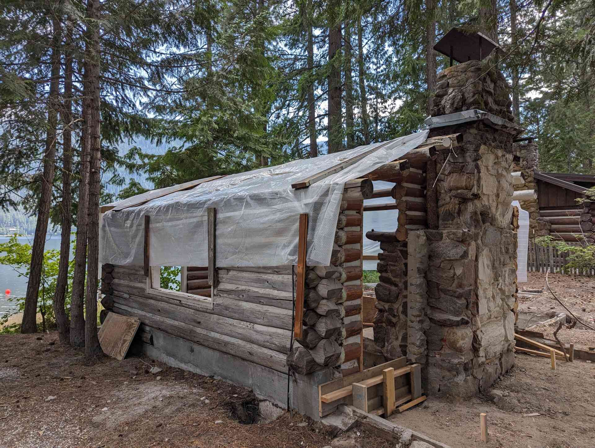 The original one-room log cabin from 1915 remains intact, revealing hand-hewn logs and a stone chimney beneath later additions. 