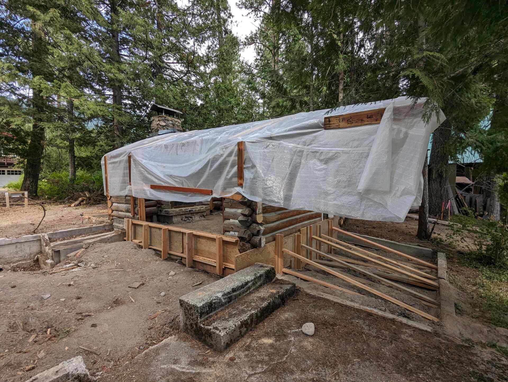 The original one-room log cabin from 1915 remains intact, revealing hand-hewn logs and a stone chimney beneath later additions. 