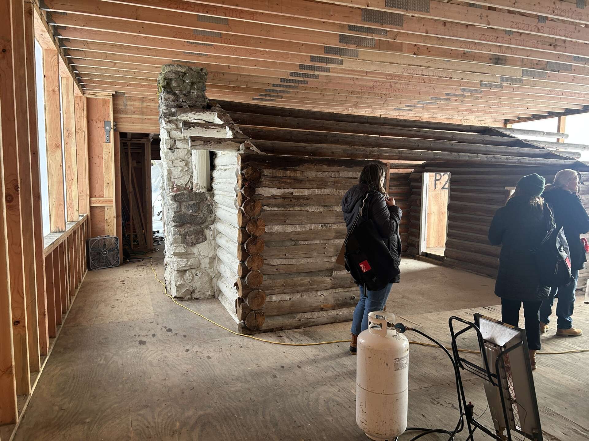 The original one-room log cabin from 1915 remains intact, revealing hand-hewn logs and a stone chimney beneath later additions. 