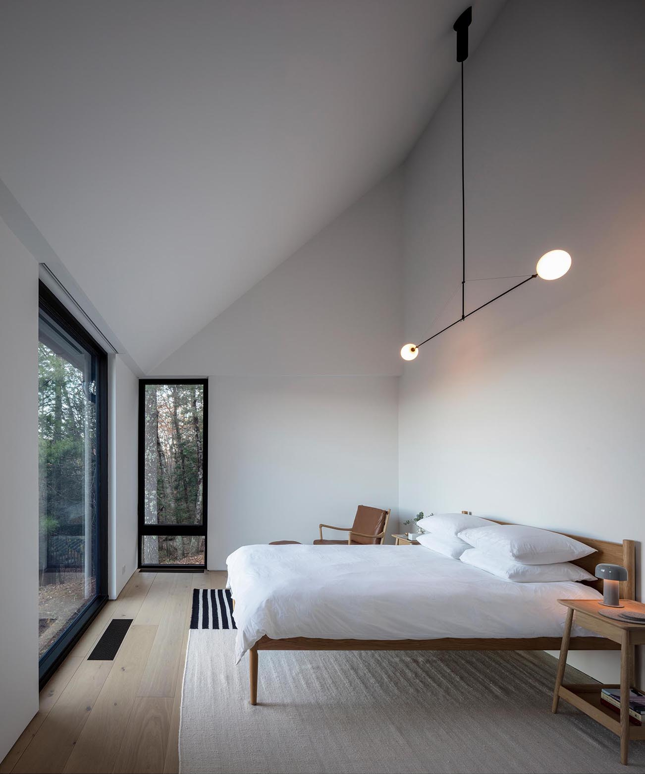 A minimalist primary bedroom with white walls, a sloped ceiling, black framed windows, and warm wood furniture that brings nature indoors.