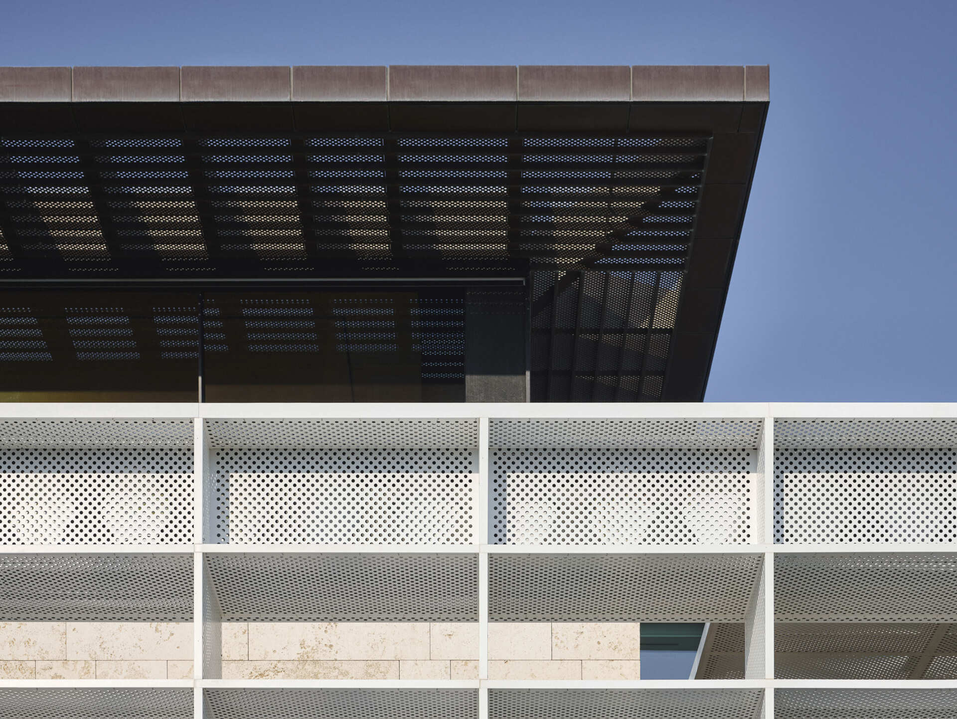 Custom copper and glass reinforced polymer screens filter light and cast shifting shadows along walkways. Carved courtyards introduce ventilation and planting, integrating passive cooling directly into the architecture.