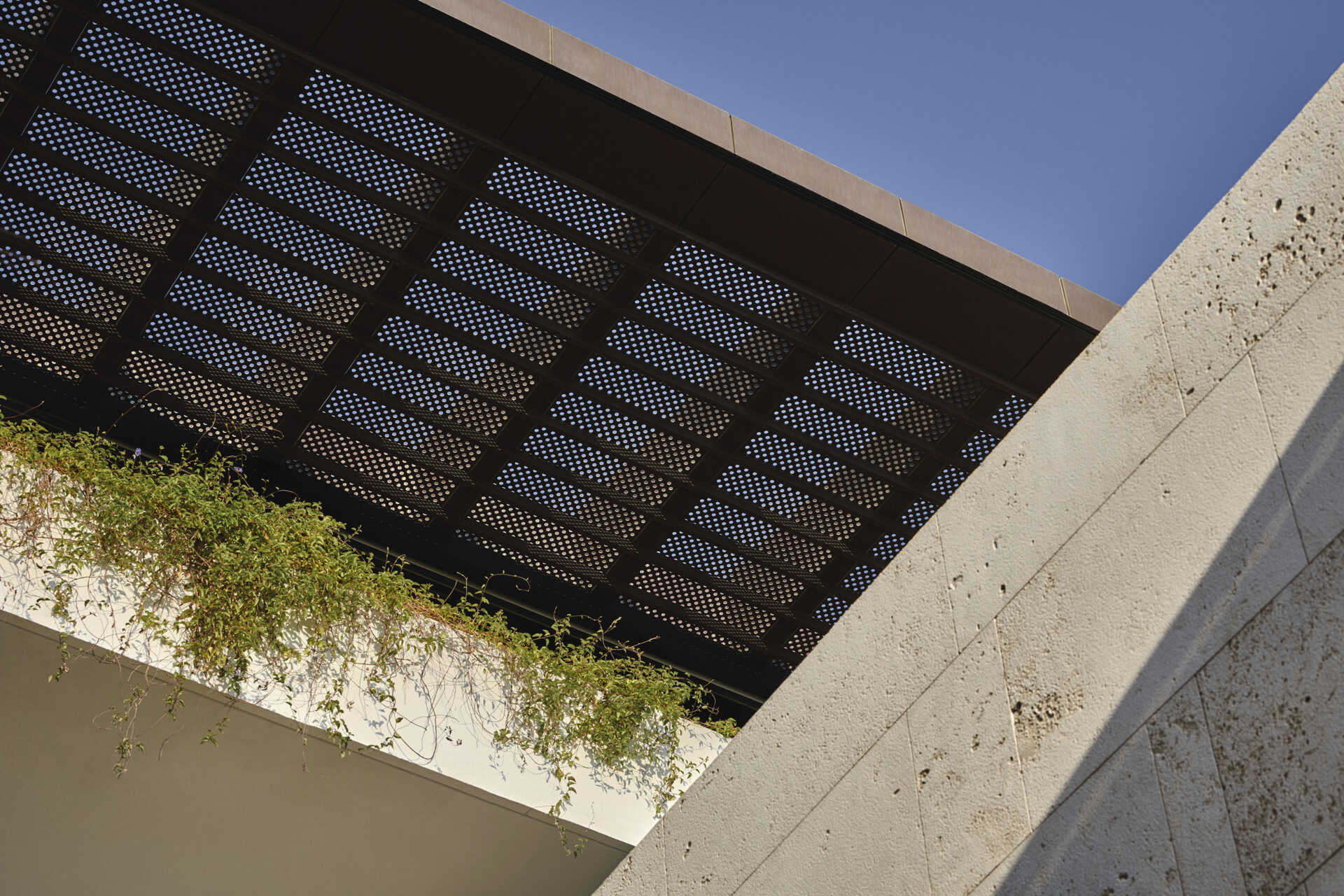 Custom copper and glass reinforced polymer screens filter light and cast shifting shadows along walkways. Carved courtyards introduce ventilation and planting, integrating passive cooling directly into the architecture.