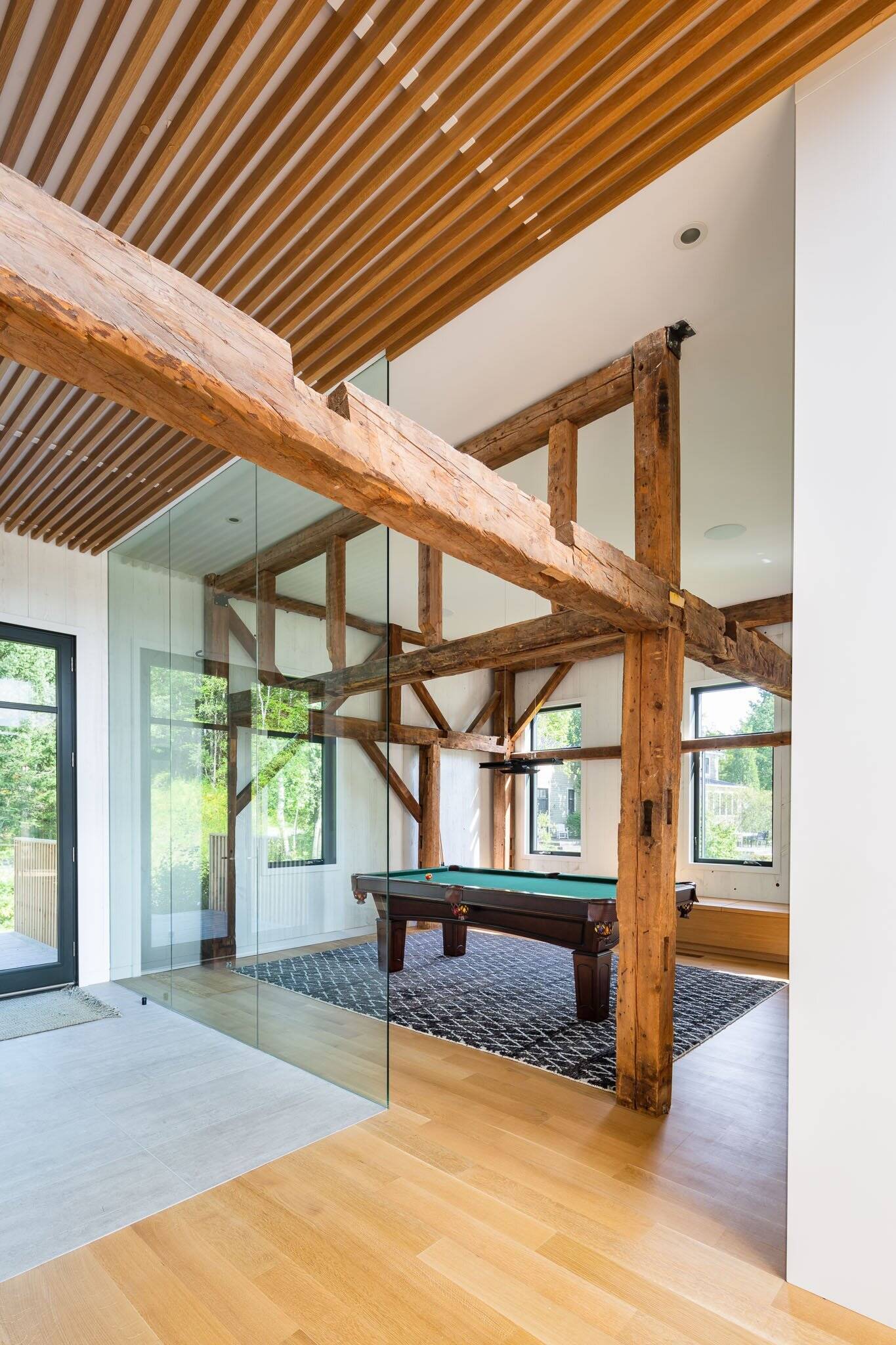 A glass walled games room with a pool table adds flexible living space inside the restored barn.