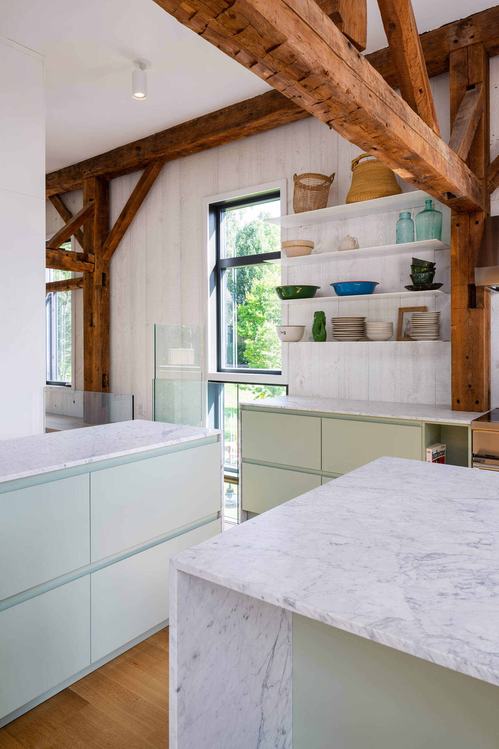 A light filled barn kitchen pairs whitewashed walls with floating shelves and soft green cabinetry.
