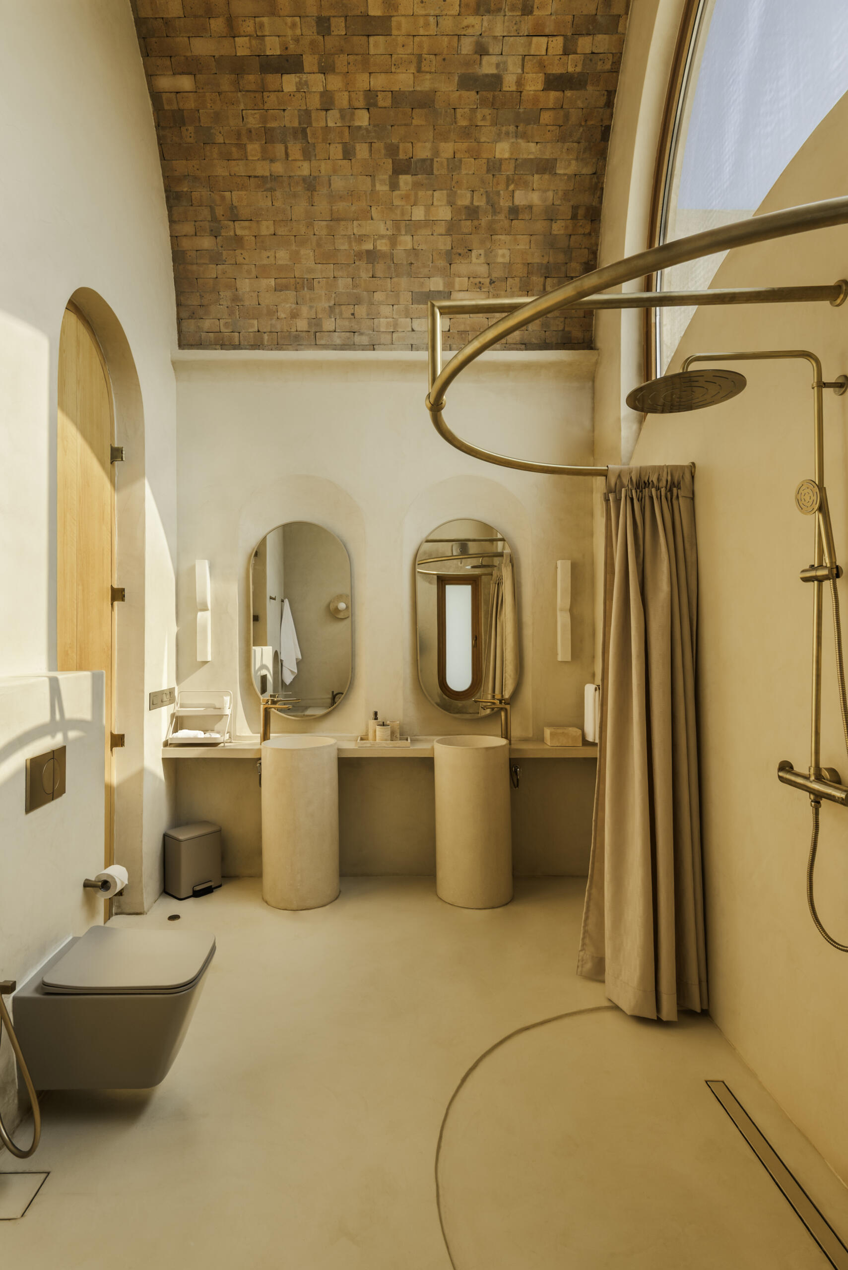 Seamless concrete curves, lime plaster walls and in-situ terrazzo basins shape cocoon-like bathrooms designed around natural light and tactile finishes.