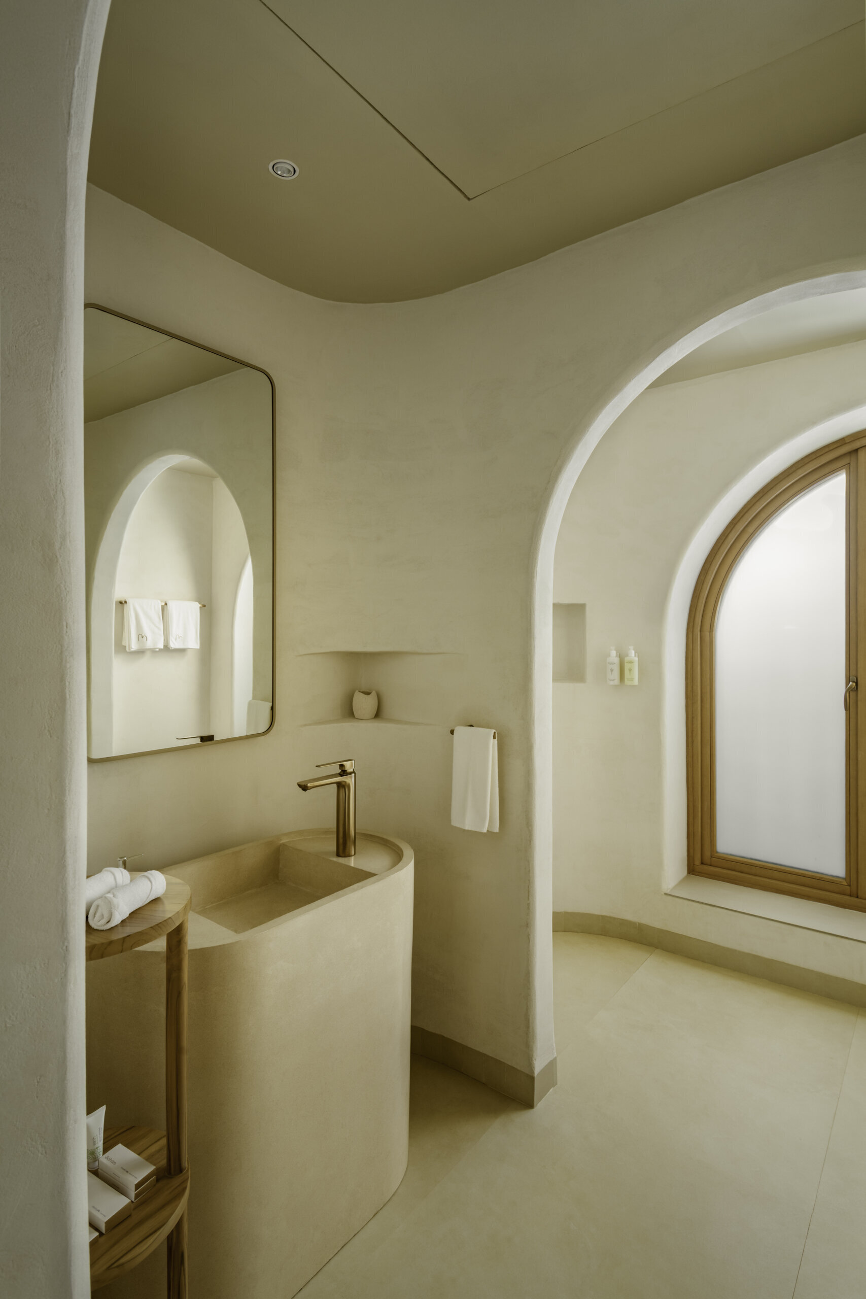 Seamless concrete curves, lime plaster walls and in-situ terrazzo basins shape cocoon-like bathrooms designed around natural light and tactile finishes.