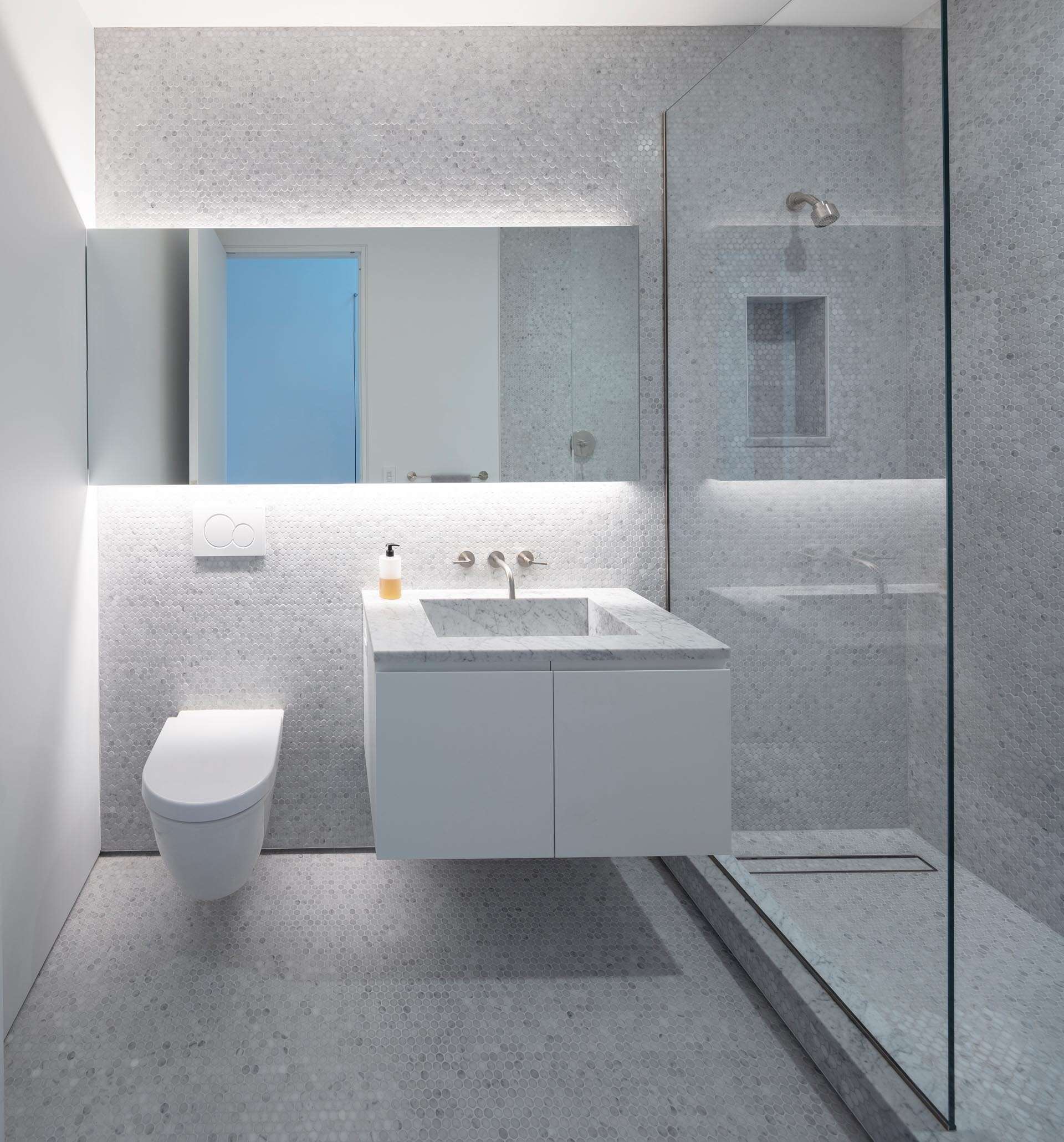 A modern bathroom finished in floor to ceiling grey penny tiles, featuring a glass shower screen and a clean, minimalist vanity area.