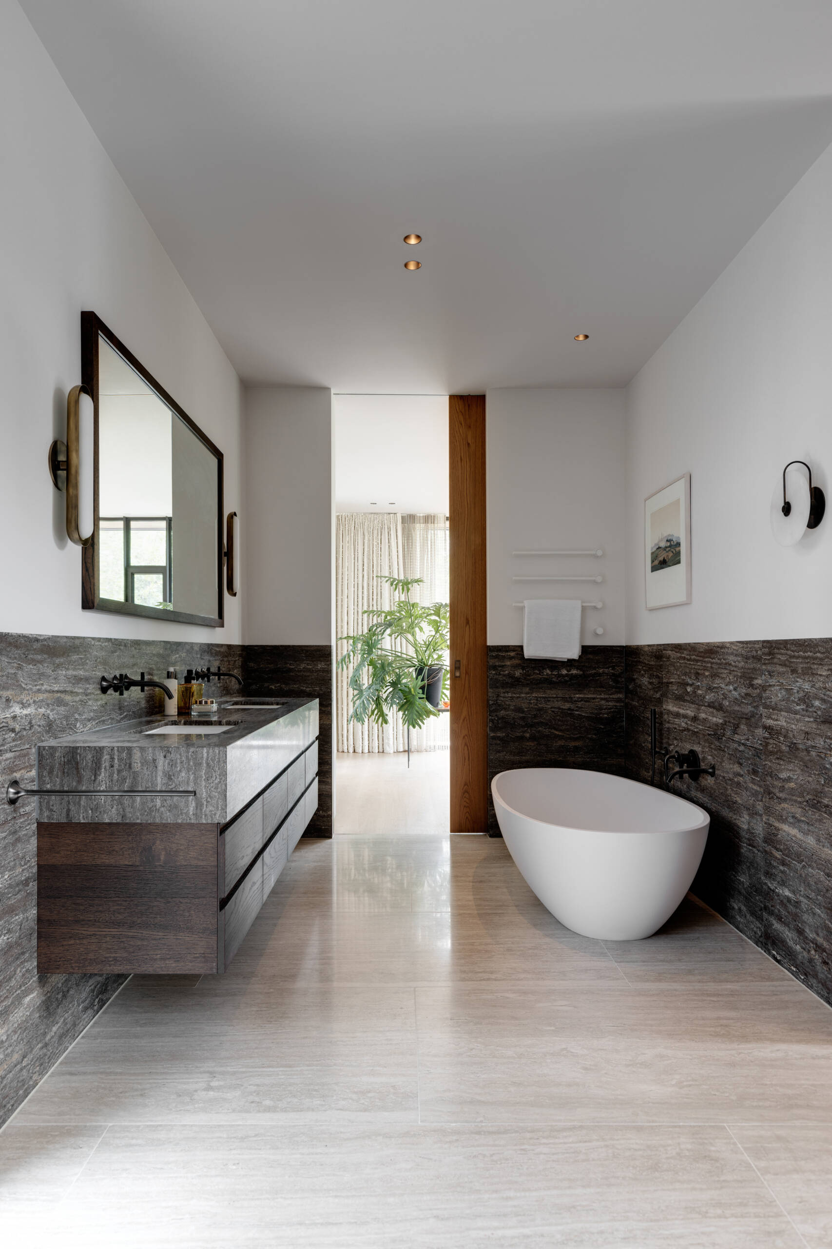 In this mid-century modern inspired bathroom, stone lines the bottom half of the walls and floor, and a window allows natural light to flow in.