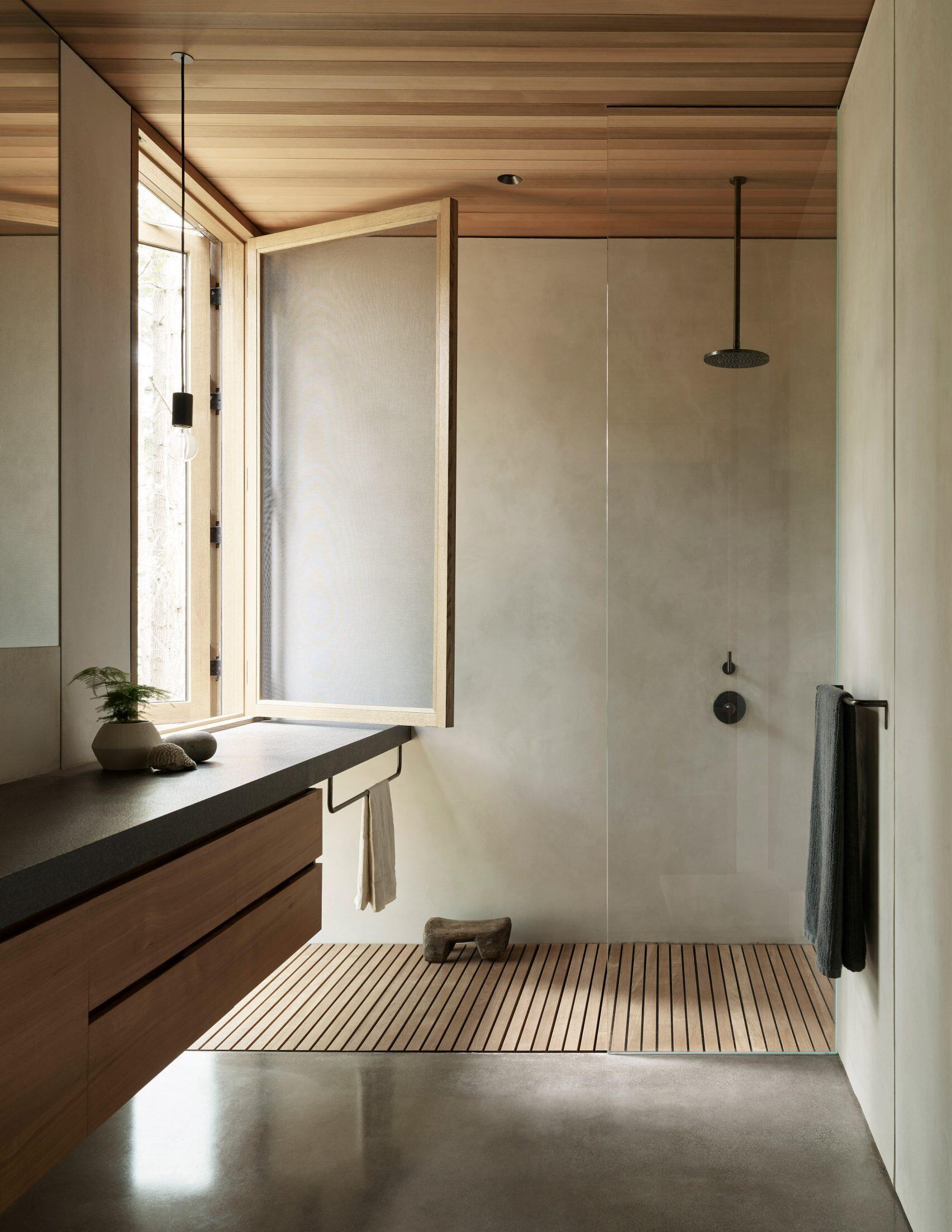 The bathroom continues the theme of natural light and warm materials. A large window brightens the shower, while a floating vanity with wood cabinetry complements the wood ceiling above. The effect is calm and cohesive, never straying far from the tones and textures of the landscape.