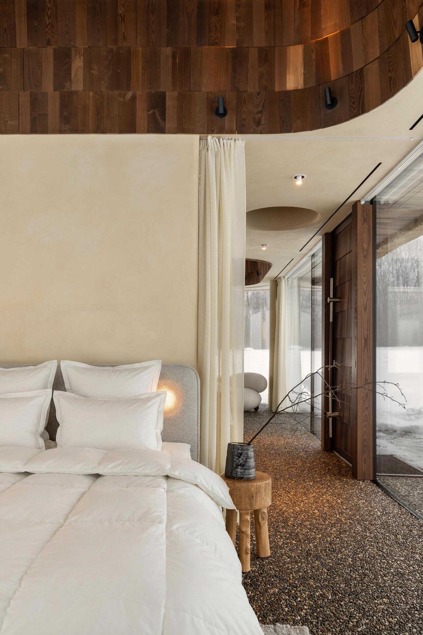 The bedroom is positioned on the opposite side of the concrete core, creating a clear and balanced layout. Floor-to-ceiling glazing keeps the space open, while privacy is handled with dense but visually light curtains. These can be closed automatically using a control panel next to the bed.