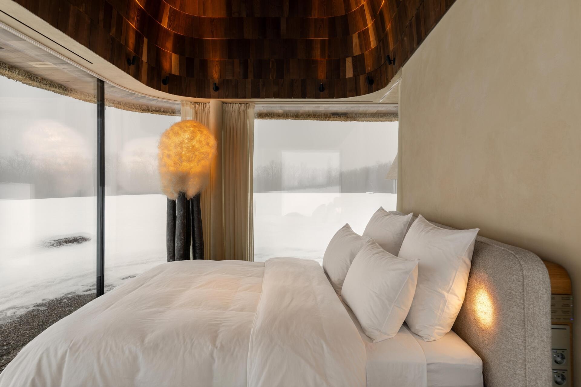 The bedroom is positioned on the opposite side of the concrete core, creating a clear and balanced layout. Floor-to-ceiling glazing keeps the space open, while privacy is handled with dense but visually light curtains. These can be closed automatically using a control panel next to the bed.