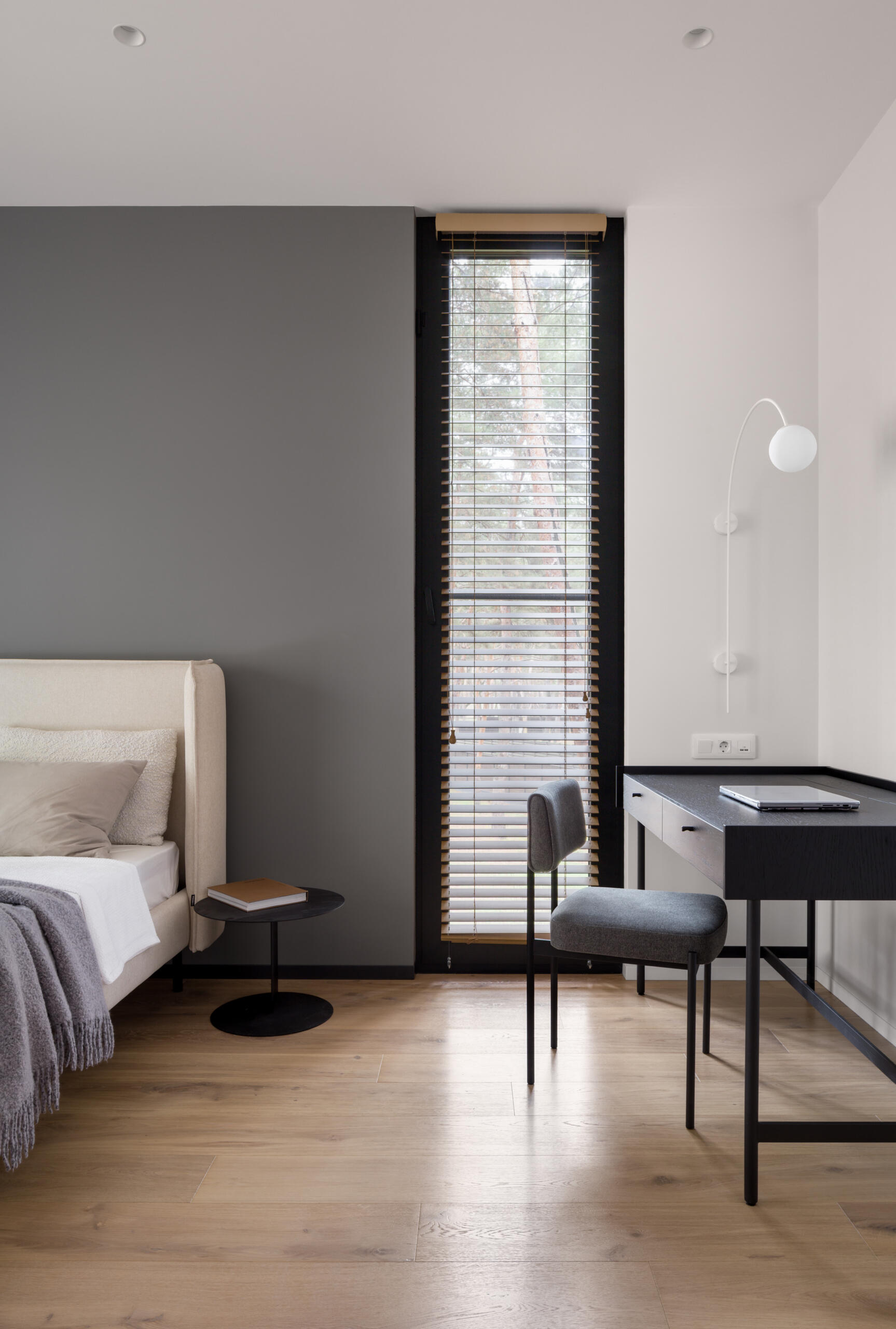 This modern bedroom is composed as a quiet space, defined by soft beige upholstery and light wood floors. Sheer curtains soften daylight from the wide glass doors and frame views of the surrounding trees.