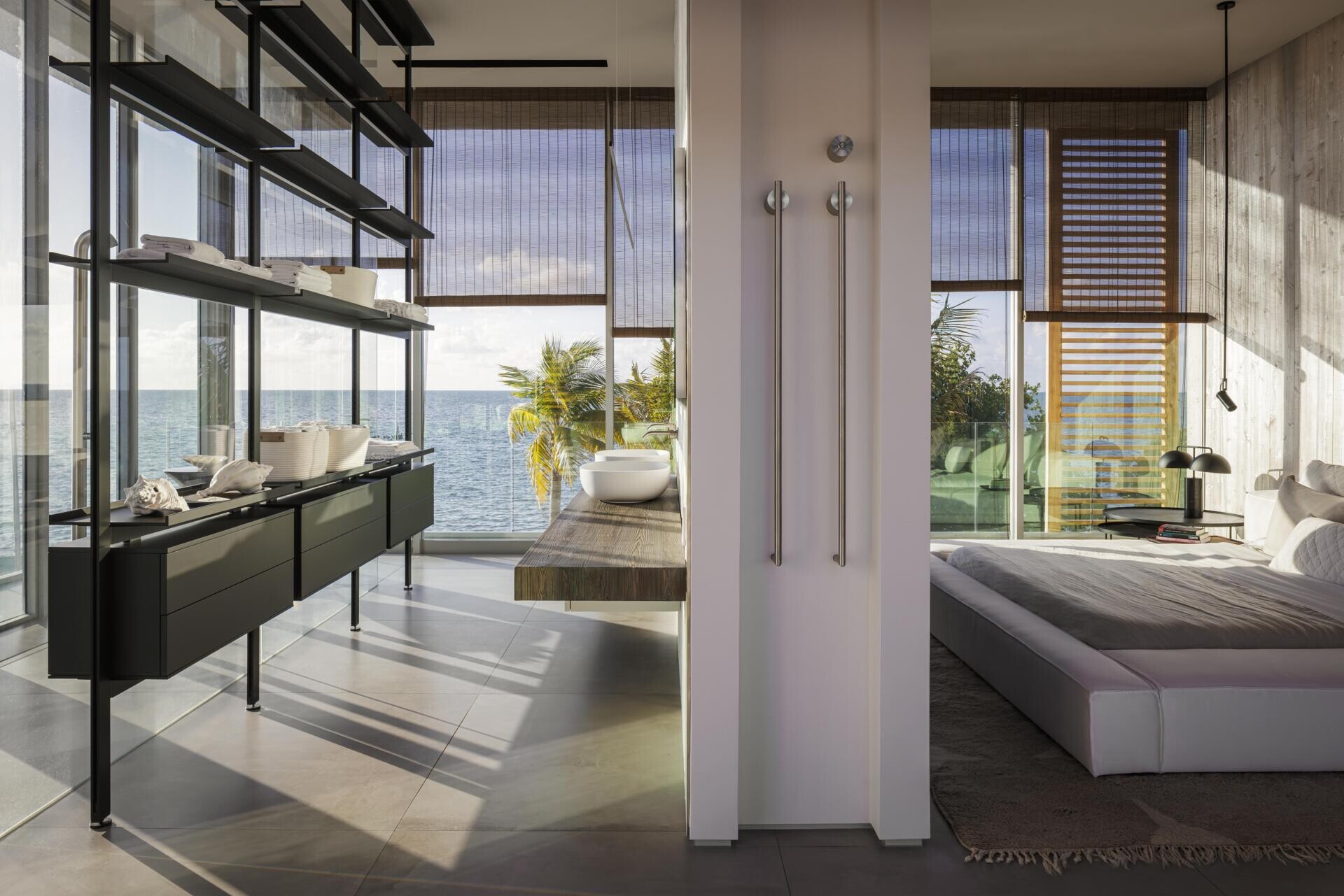 The primary suite features sliding glass walls and textured concrete details with expansive water views.