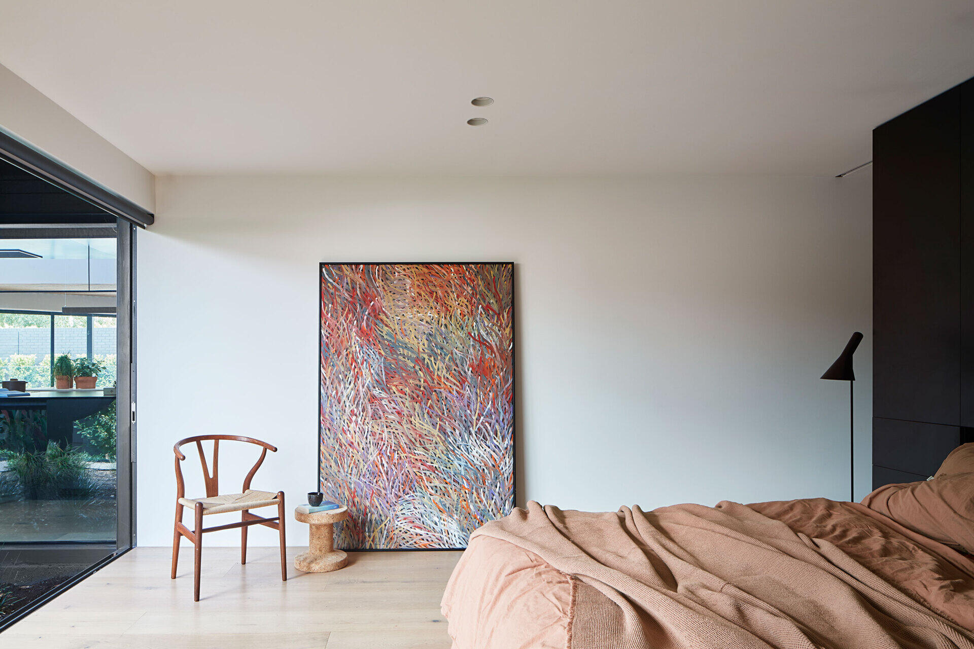 A bold black accent wall frames the bed and opens toward a small garden, creating a calm and grounded sleeping space.