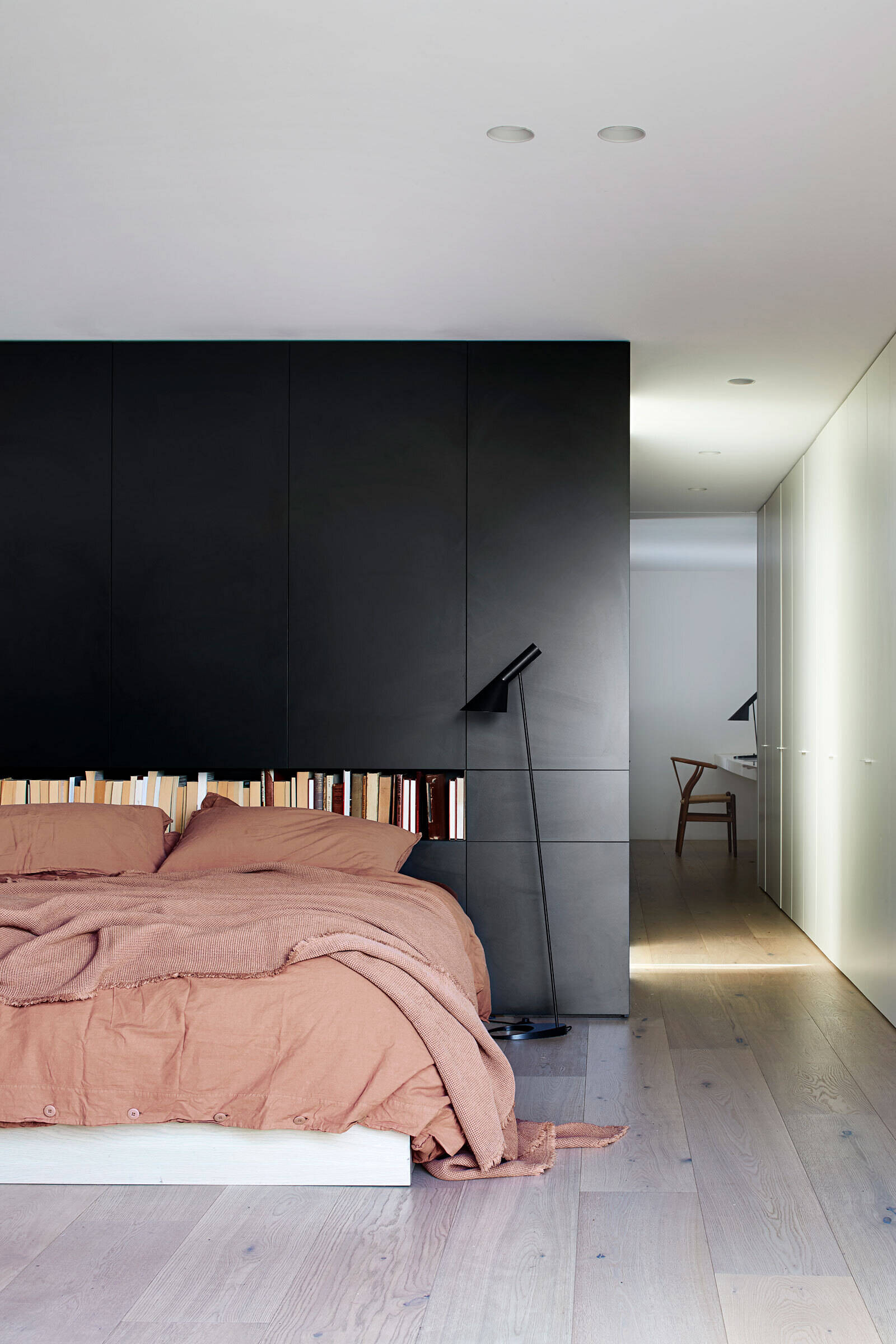 A bold black accent wall frames the bed and opens toward a small garden, creating a calm and grounded sleeping space.