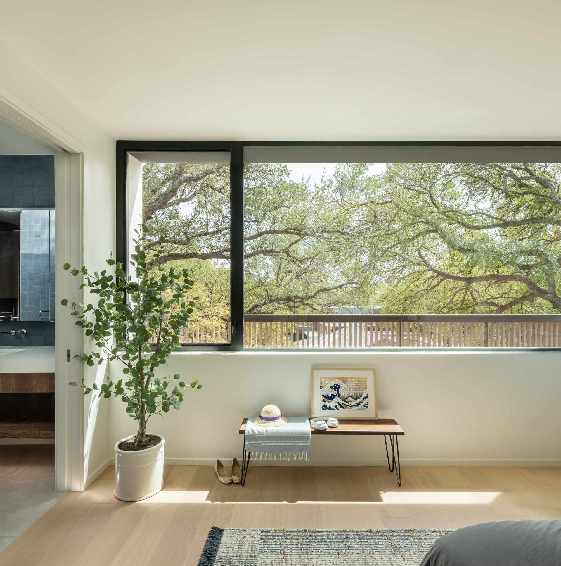 The primary suite continues the theme of measured openness. Positioned to take advantage of privacy and long views, it feels connected to the layered landscape beyond. The ensuite bathroom features a square blue tile accent wall below a skylight, while a double vanity lines the opposite wall.