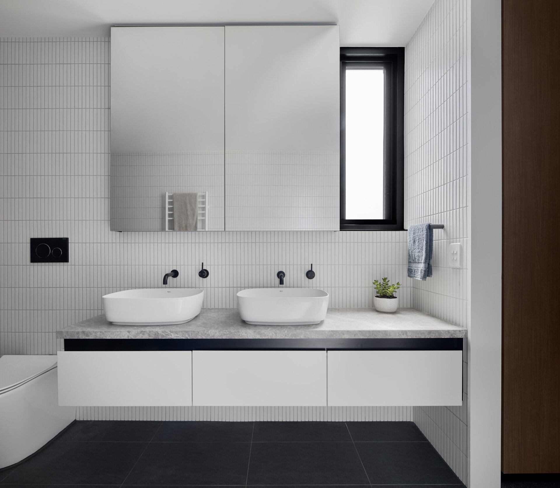 Black shower tiles paired with hidden niche lighting create a bold focal point, contrasted by crisp white finishes throughout the rest of the bathroom.