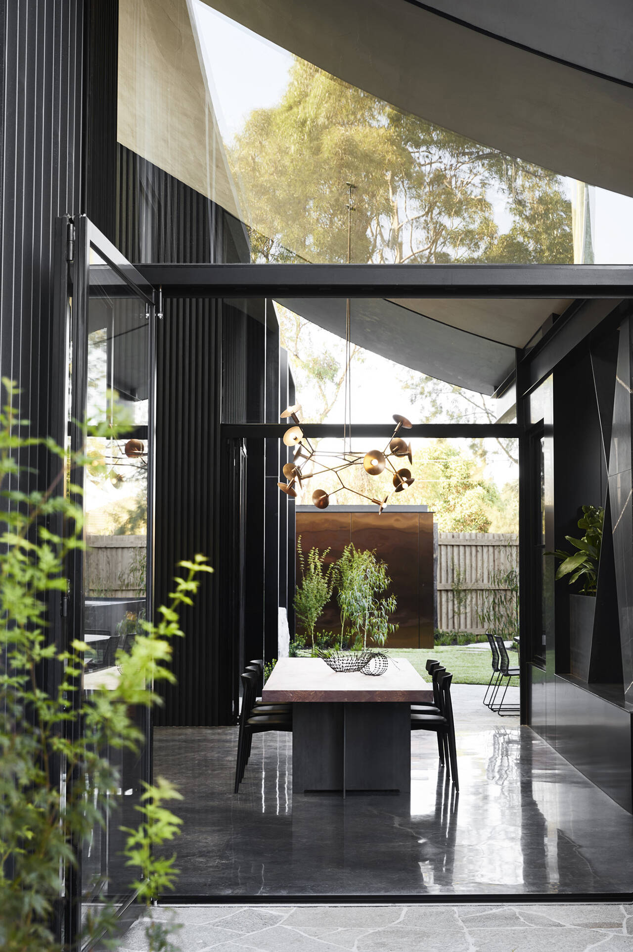 A sculptural light fixture anchors the dining area, suspended above a wood and black metal table. Glamour meets industrial influence in this striking open plan space.