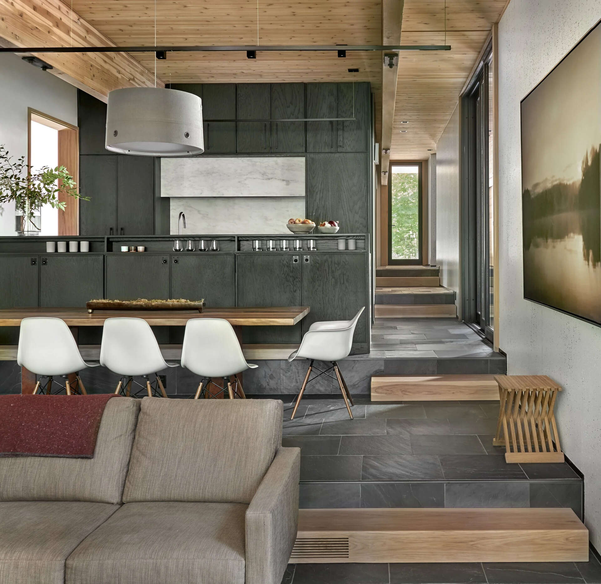 Dark stained oak cabinets and black slate floors define a terraced kitchen and dining space that follows the natural slope of the land.