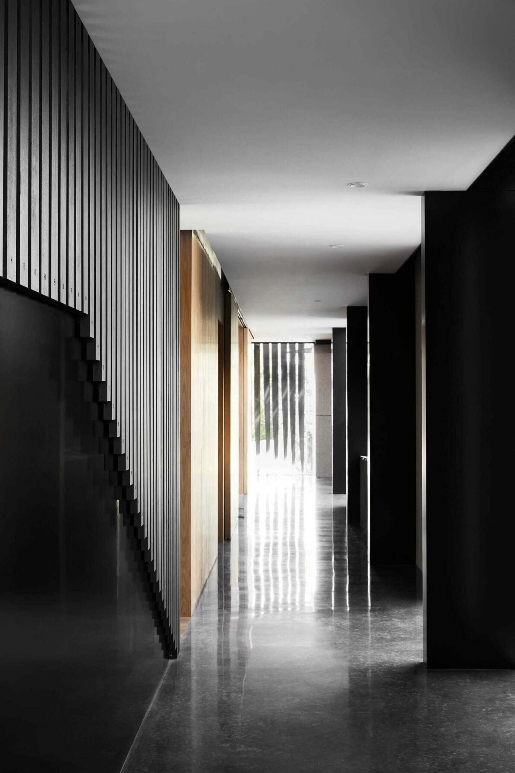 A long hallway lined with blackened timber slats sets a moody tone from the moment you step inside. The rhythmic design leads from the entry to the open plan living spaces.