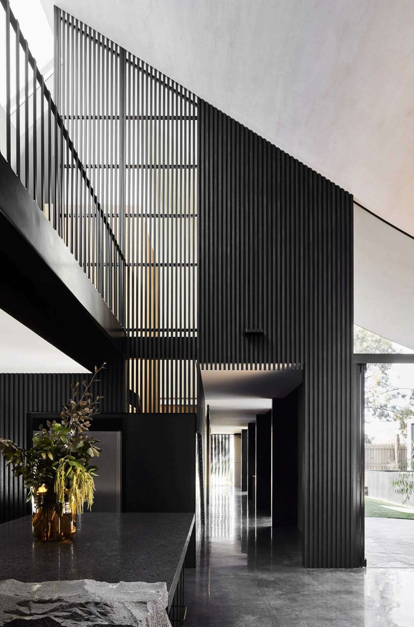 A long hallway lined with blackened timber slats sets a moody tone from the moment you step inside. The rhythmic design leads from the entry to the open plan living spaces.
