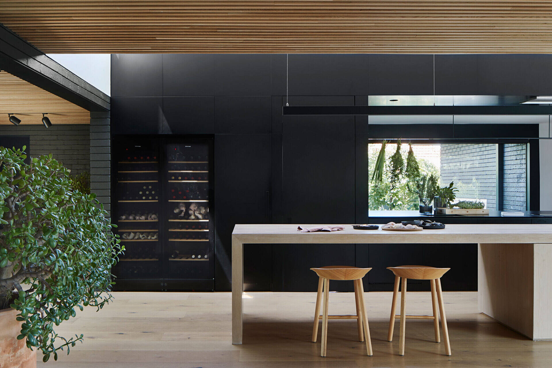 Minimal black cabinetry and a generous island define this kitchen, with clever voids allowing connection to the pantry beyond.