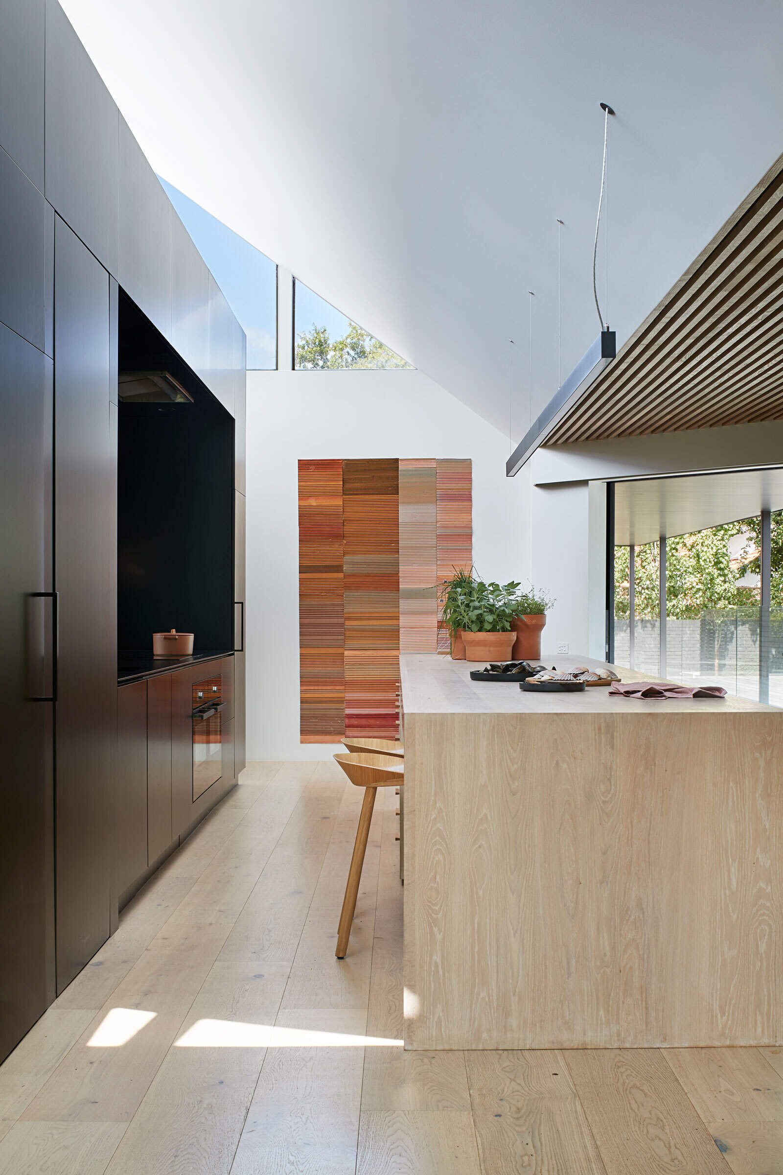 Minimal black cabinetry and a generous island define this kitchen, with clever voids allowing connection to the pantry beyond.