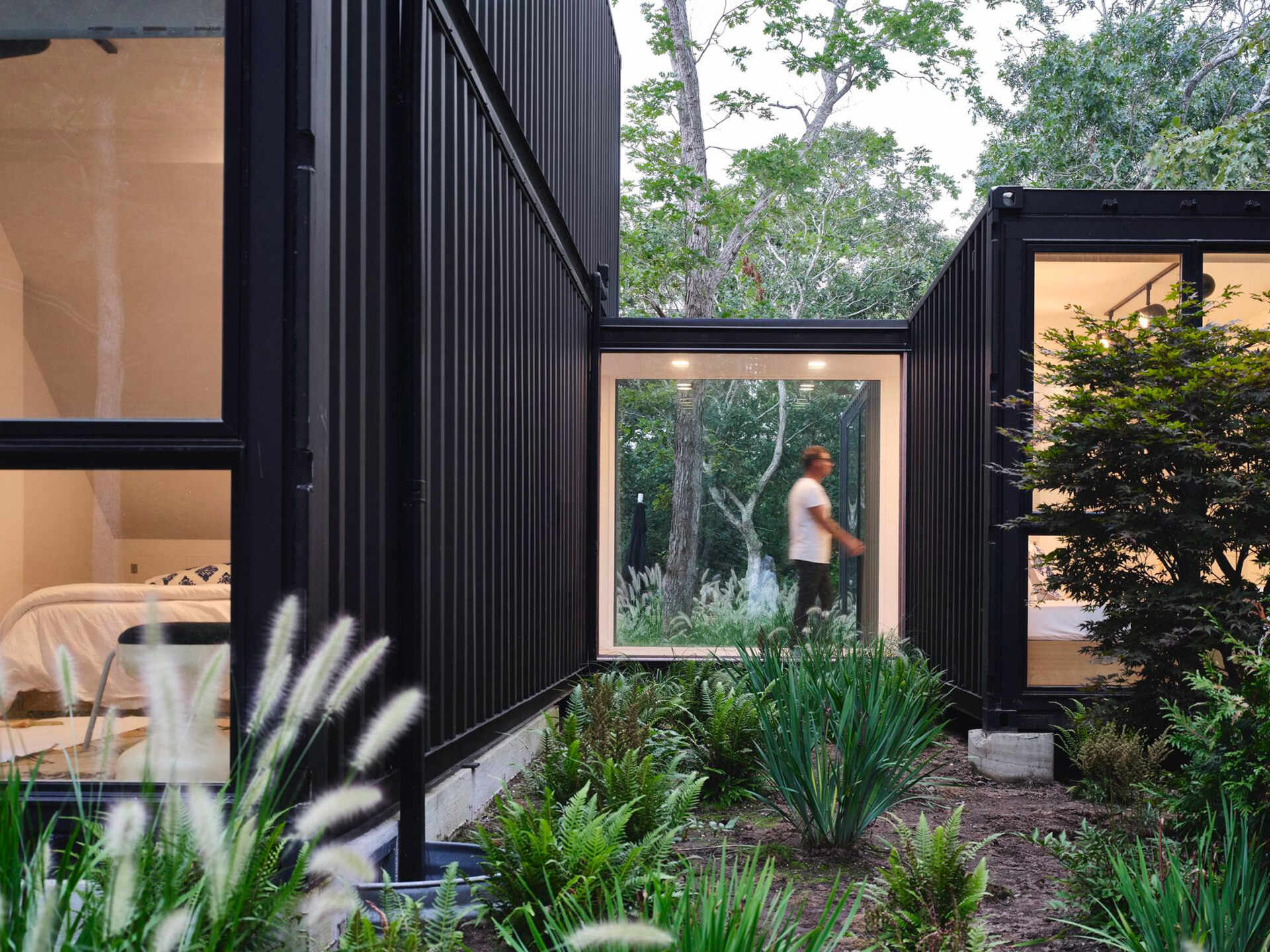A window-lined bridge links the main house to a separate two-bedroom container, forming courtyard-like outdoor spaces in between. A clever layout that maximises privacy and openness at once.