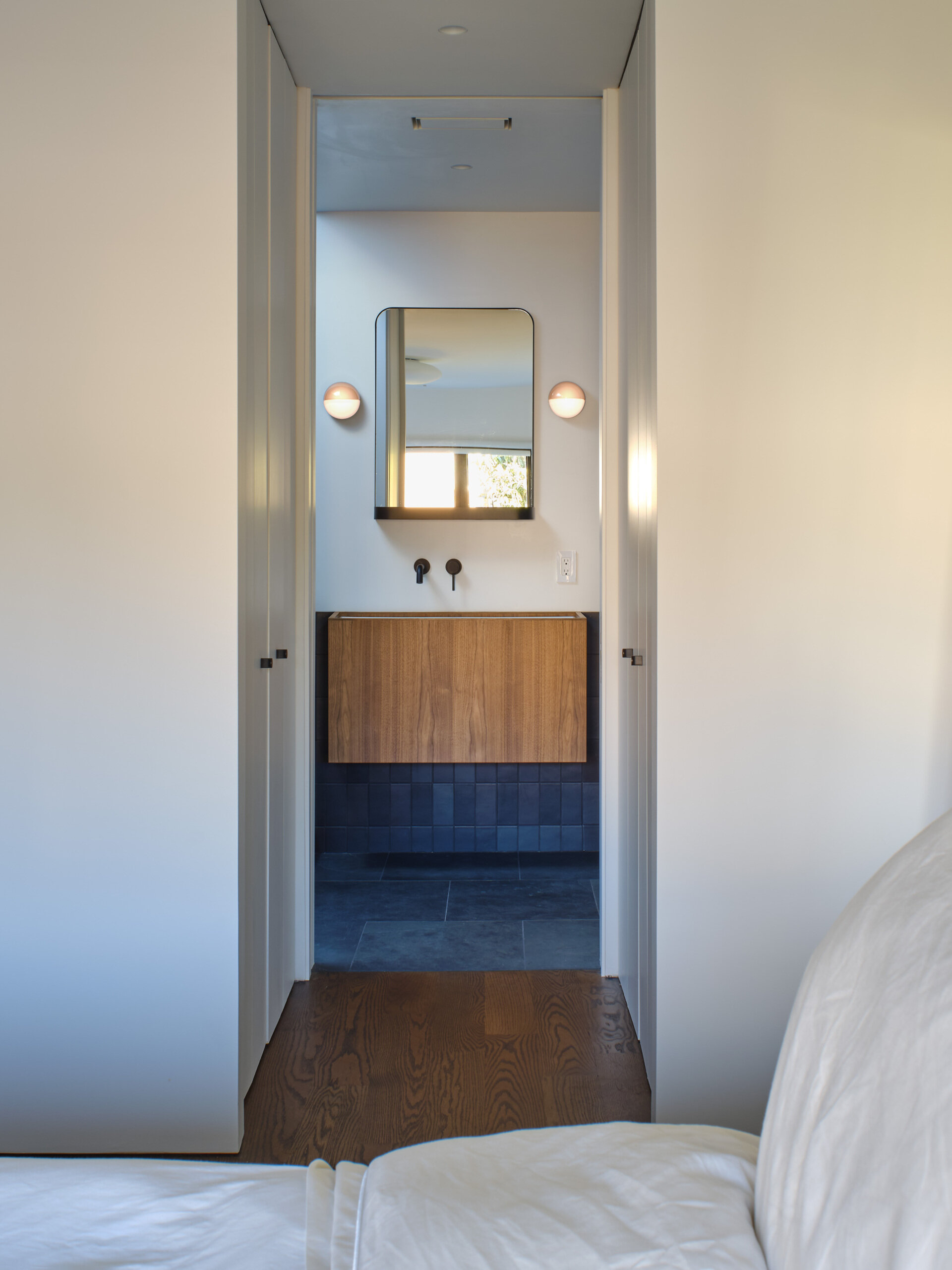 Like many older homes, the bathrooms were previously dark and enclosed. Natural light was minimal. The reconfigured main bathroom introduces a dramatic skylight directly over the shower. Dark gray tiles, slate flooring, and walnut cabinetry create contrast beneath the daylight above.