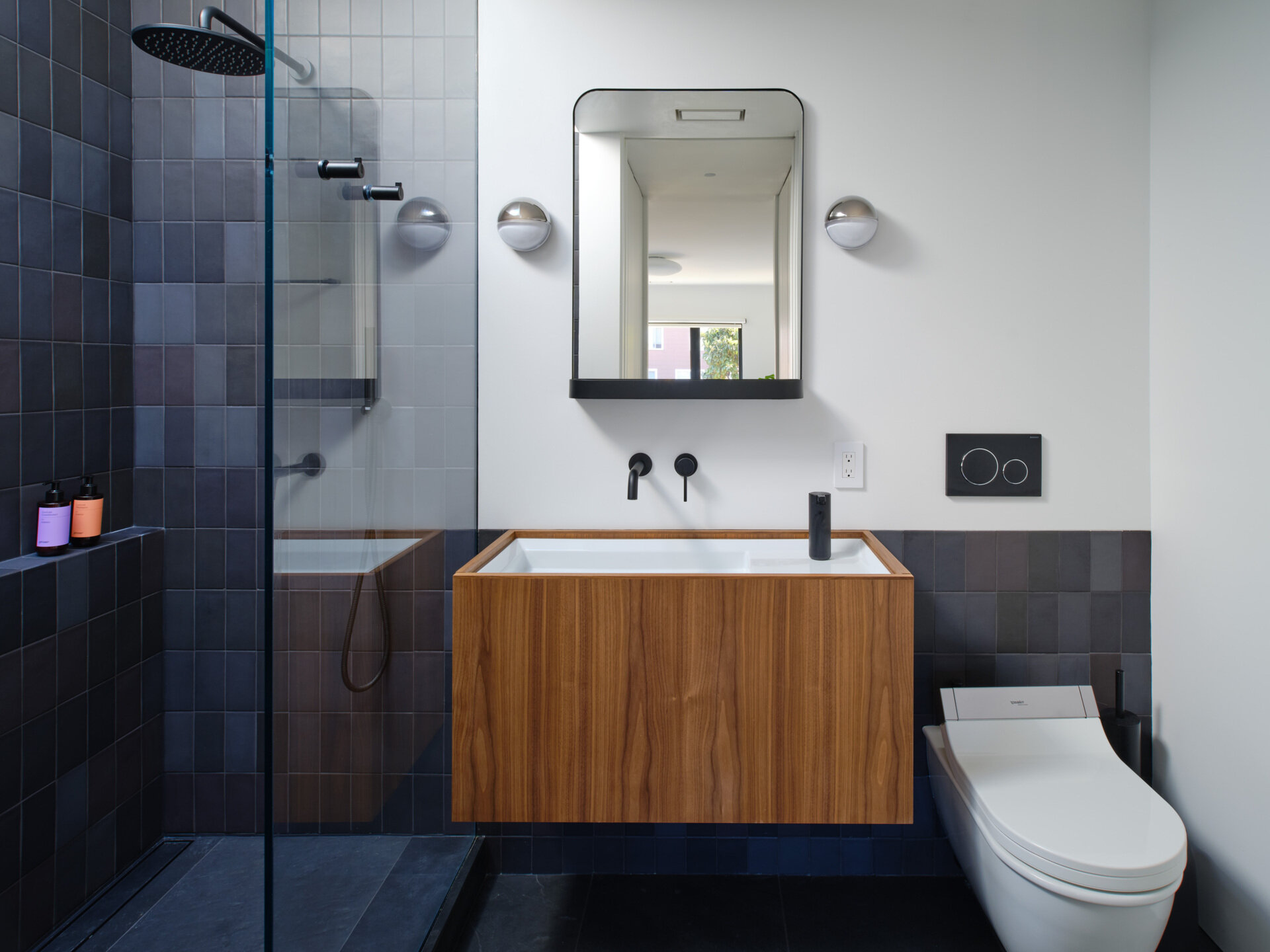 Like many older homes, the bathrooms were previously dark and enclosed. Natural light was minimal. The reconfigured main bathroom introduces a dramatic skylight directly over the shower. Dark gray tiles, slate flooring, and walnut cabinetry create contrast beneath the daylight above.