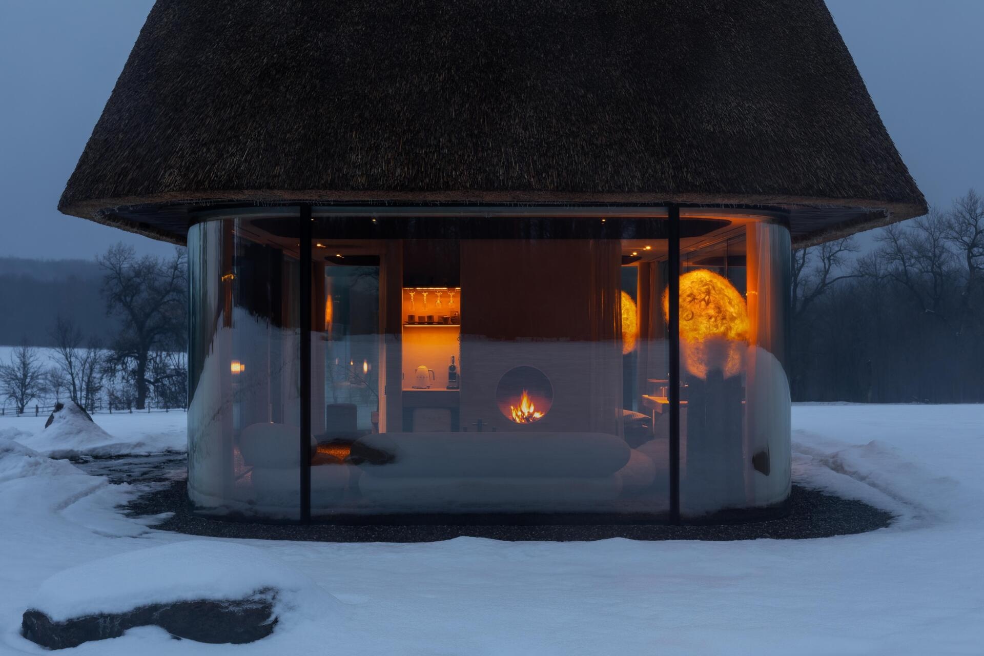 These glass guesthouses use an oversized thatched roof and transparent walls to redefine a traditional house form.