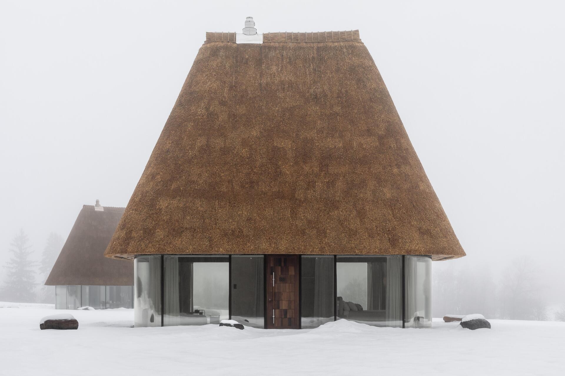 These glass guesthouses use an oversized thatched roof and transparent walls to redefine a traditional house form.