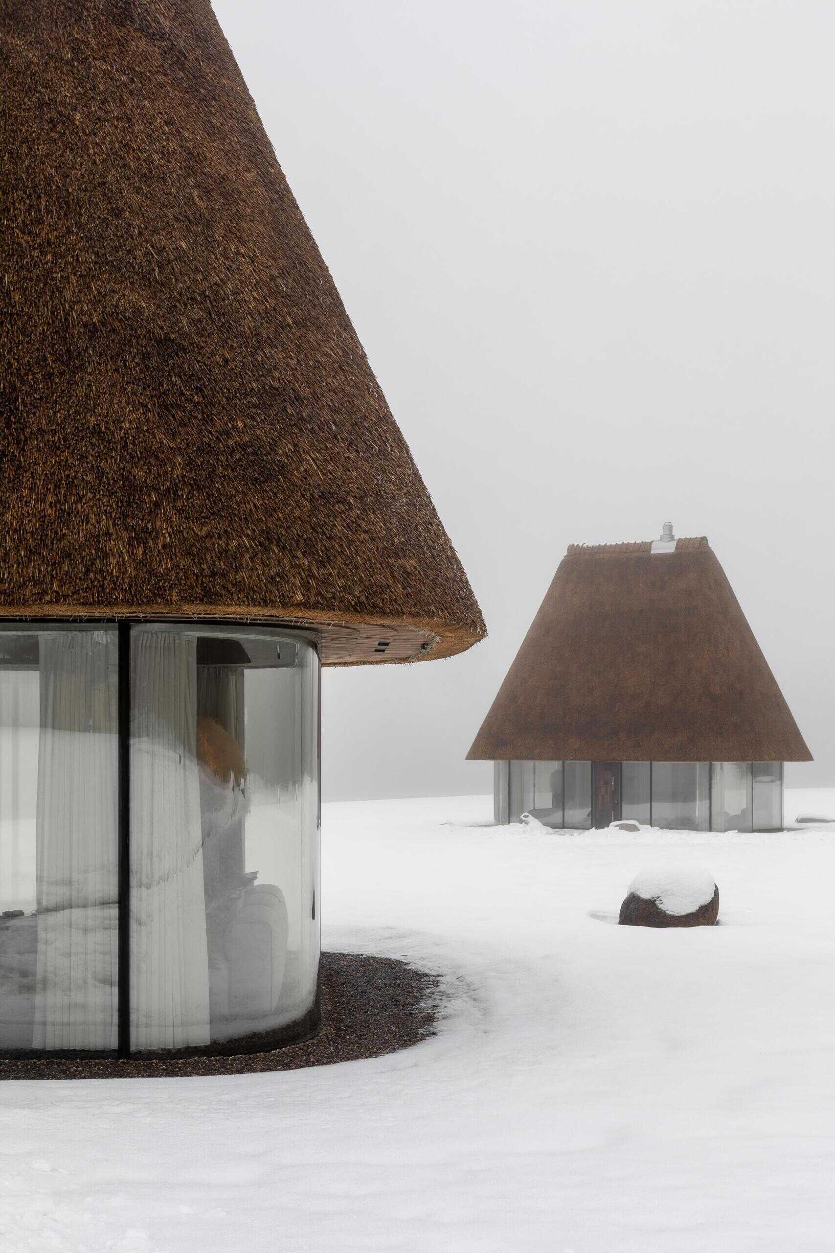 These glass guesthouses use an oversized thatched roof and transparent walls to redefine a traditional house form.
