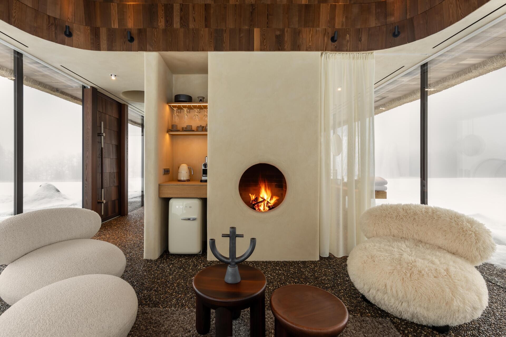 Inside, the living room sits on one side of a central concrete core. The space is deliberately simple, with a minimalist built-in fireplace as the main focal point.

There is no television. The idea is to replace screens with fire and views, encouraging guests to slow down and stay visually connected to what is happening outside.