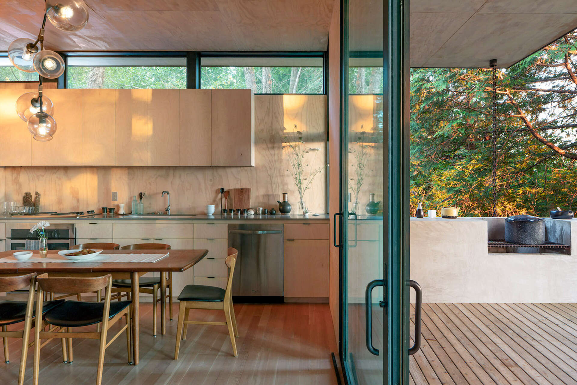 A pass through kitchen window extends the countertop outdoors, connecting cooking, dining, and social life with the surrounding landscape.
