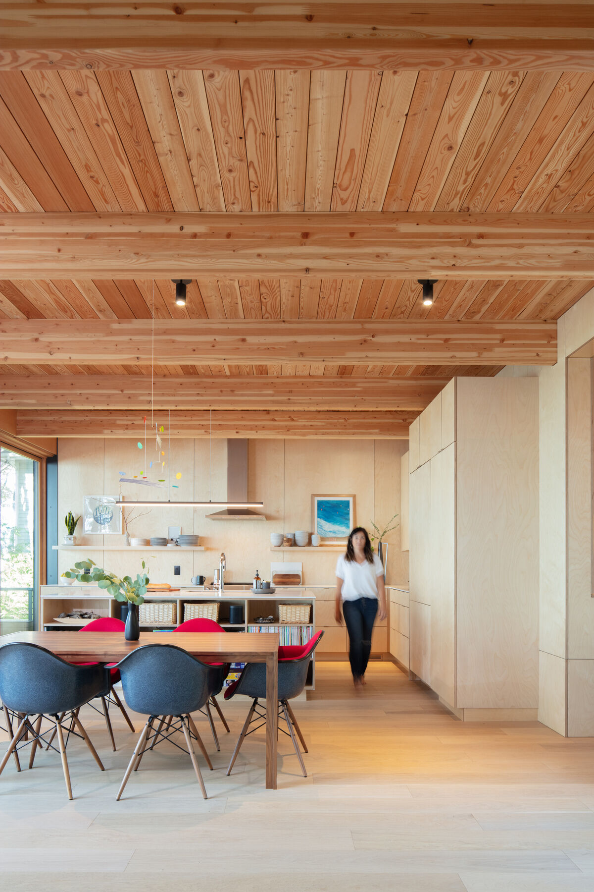 This airy kitchen leans into a soft, natural palette, with pale wood cabinetry and wide-plank floors that keep everything feeling light and easy. The standout ceiling, lined in warm wood boards and beams, adds texture overhead, especially with the simple black spotlights.