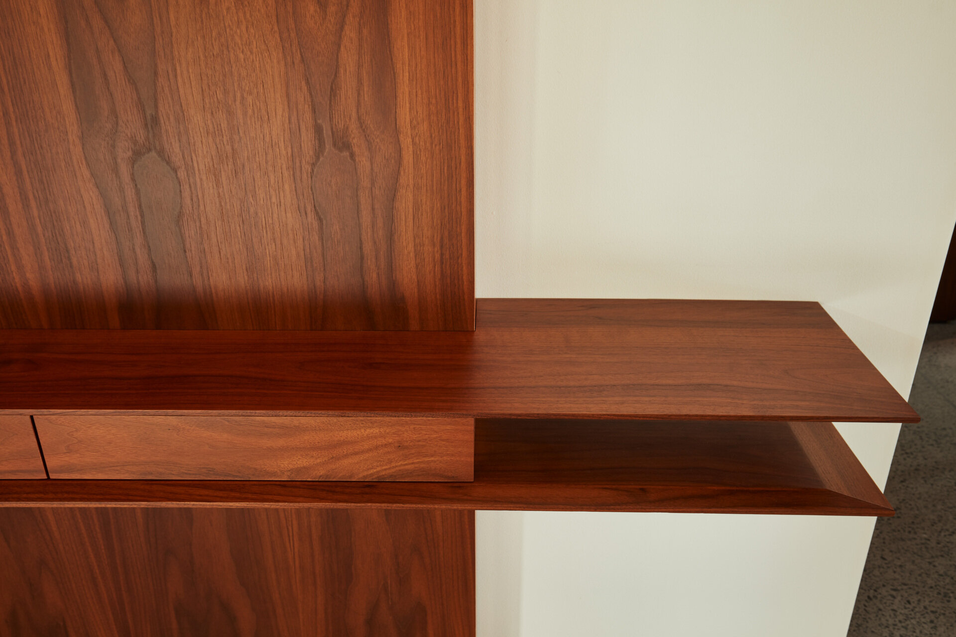 En el interior, la historia de los materiales continúa con las superficies de madera que resultan cálidas y duraderas. Los estantes de madera con cajones ocultos añaden una funcionalidad sutil a la entrada, proporcionando almacenamiento sin destruir la simplicidad del espacio.