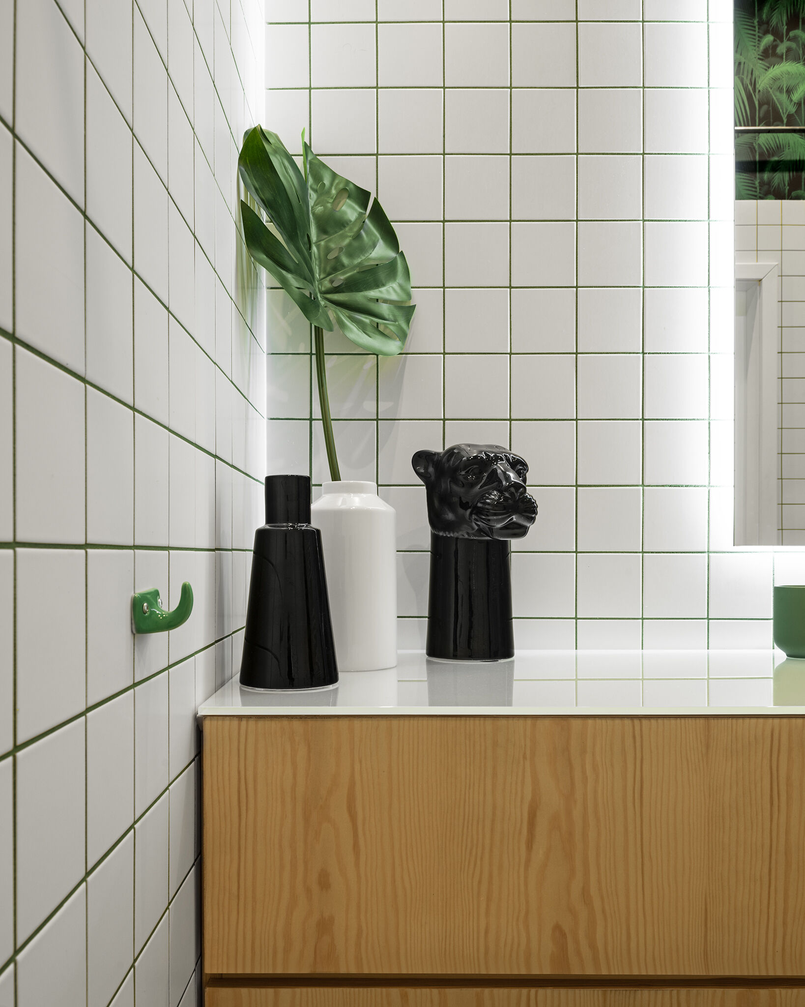 A clean and character filled bathroom with white tiles, a wood vanity, palm patterned walls, and softly back lit mirrors.