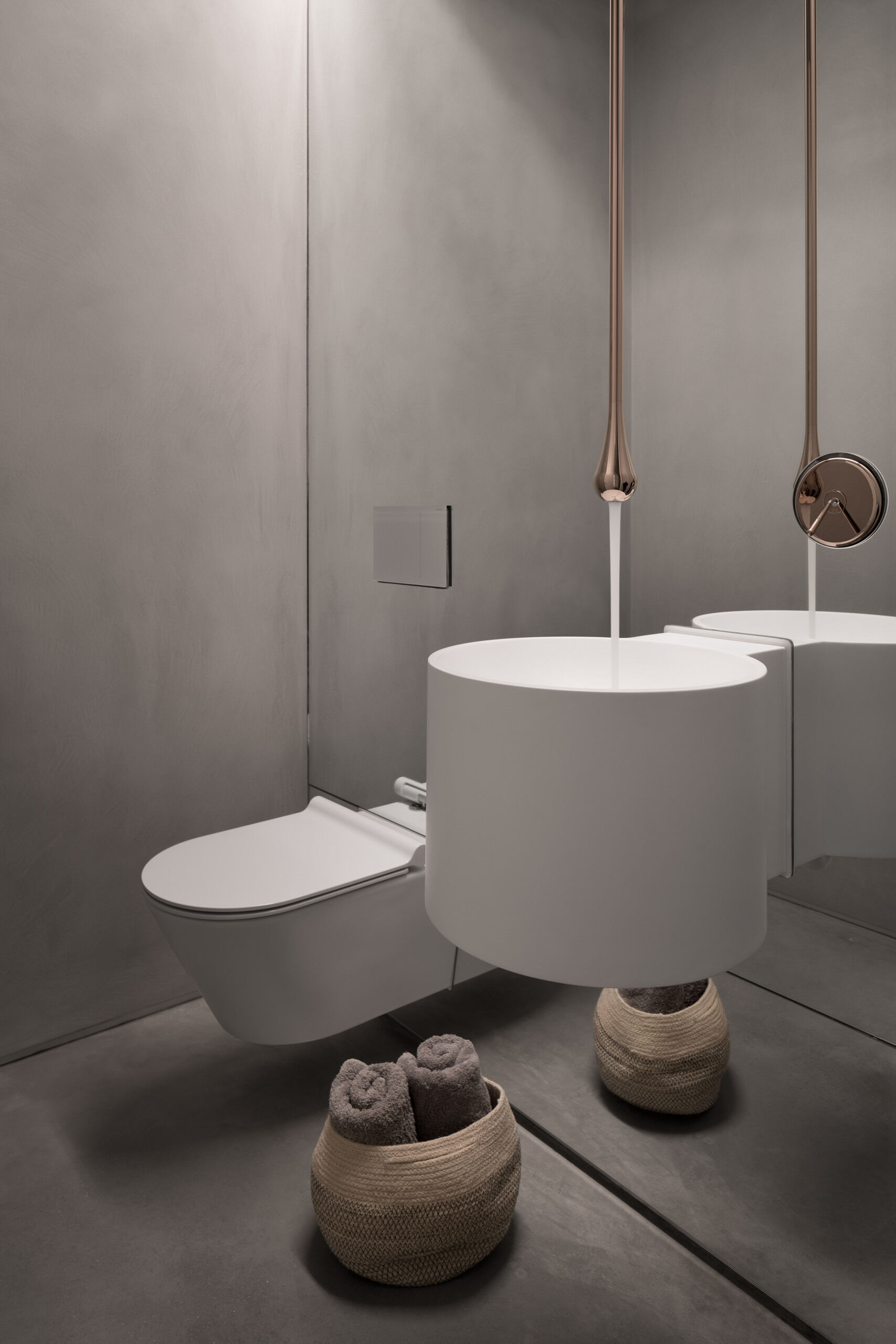 Grey walls, a full height mirror, and a ceiling mounted faucet create a striking and unexpected bathroom interior.