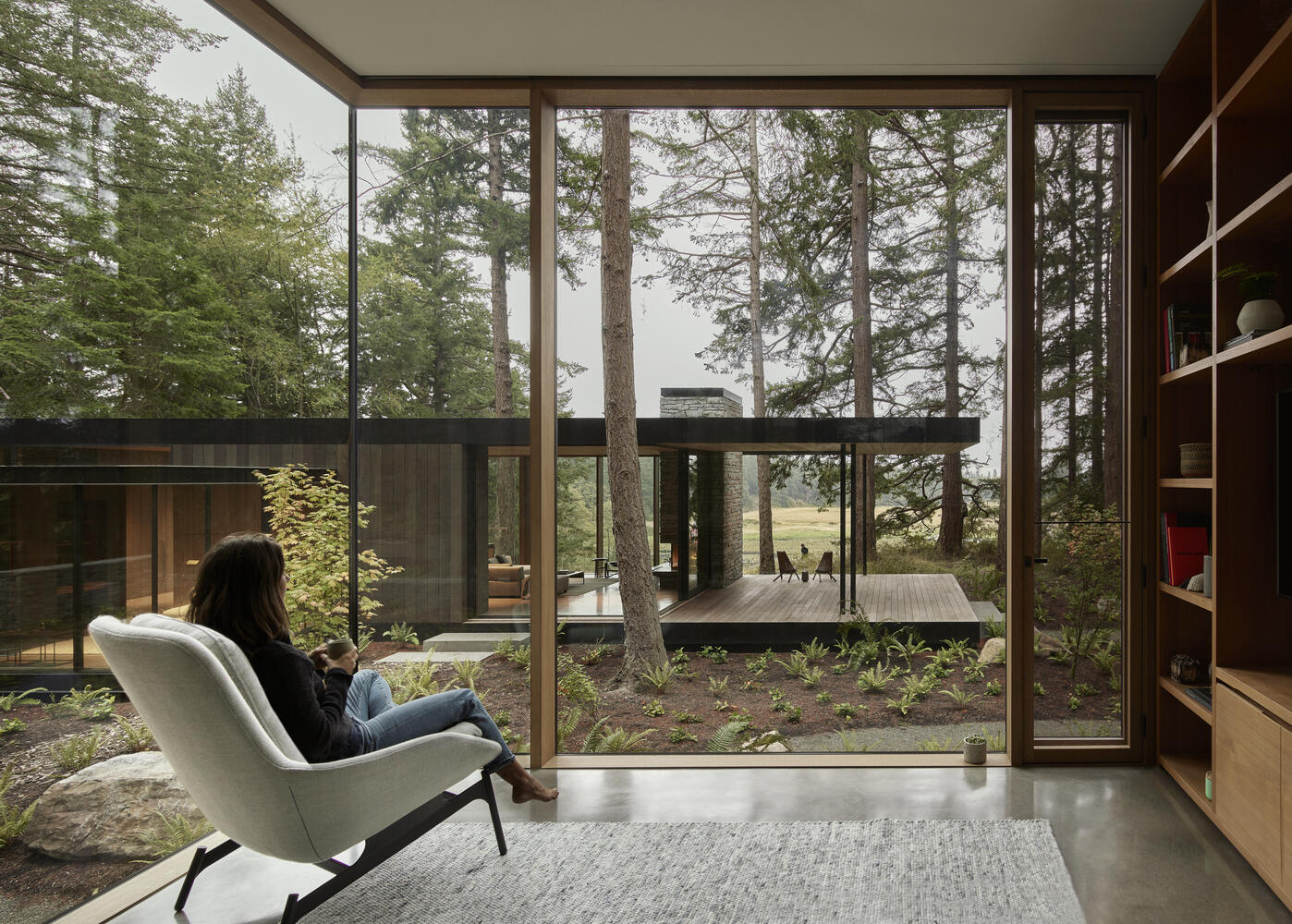 This separate building houses a library and looks onto a courtyard filled with native shrubs and ferns. Surrounded by large Douglas Fir trees, it feels private yet still connected. The arrangement allows family members to gather together or retreat into quieter corners when needed.